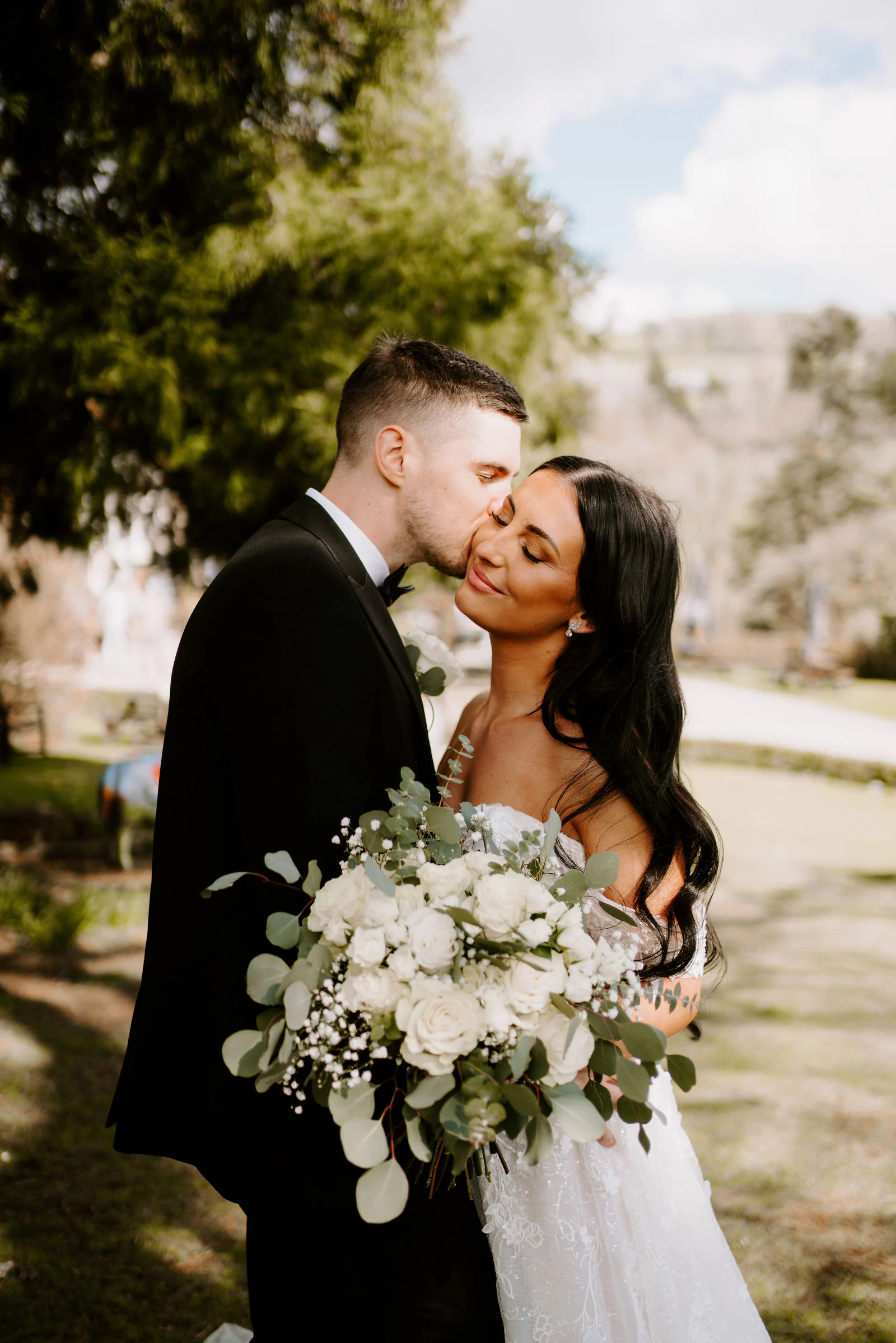 A groom kisses the bride's cheek in the gardens at Broadoaks Country House