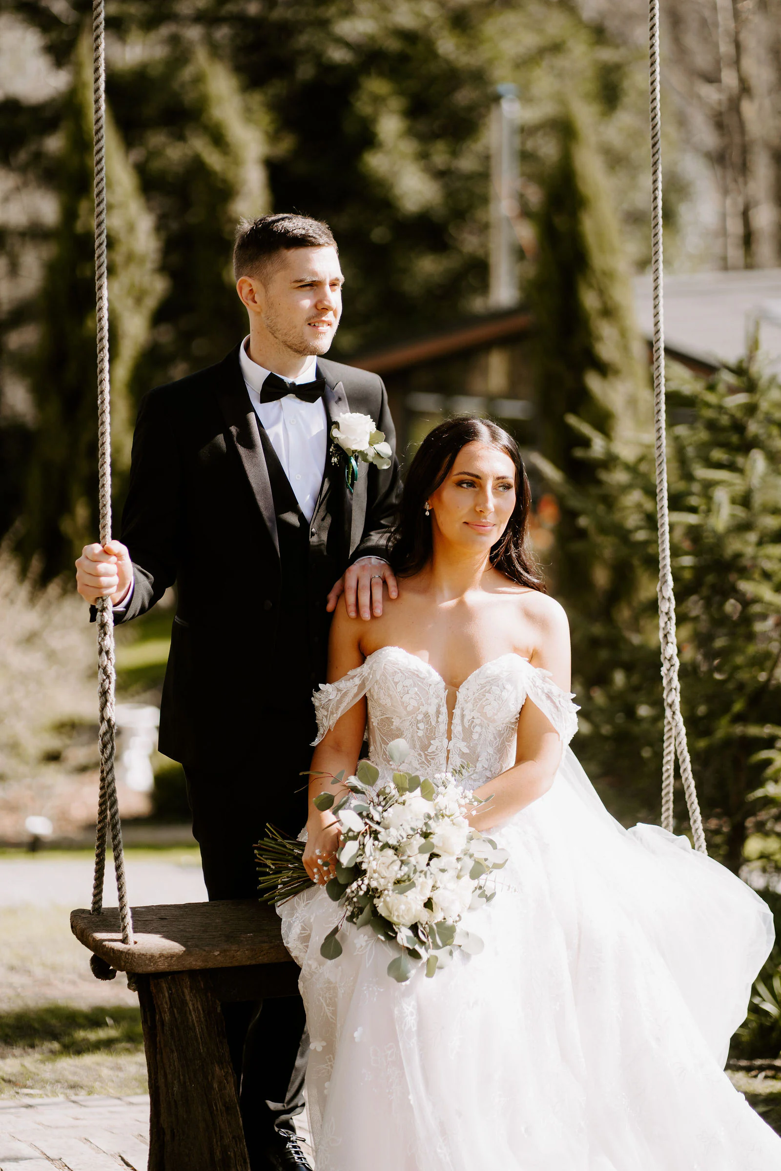 A bride and groom sit together on a wooden swing in the gardens at Broadoaks Country House