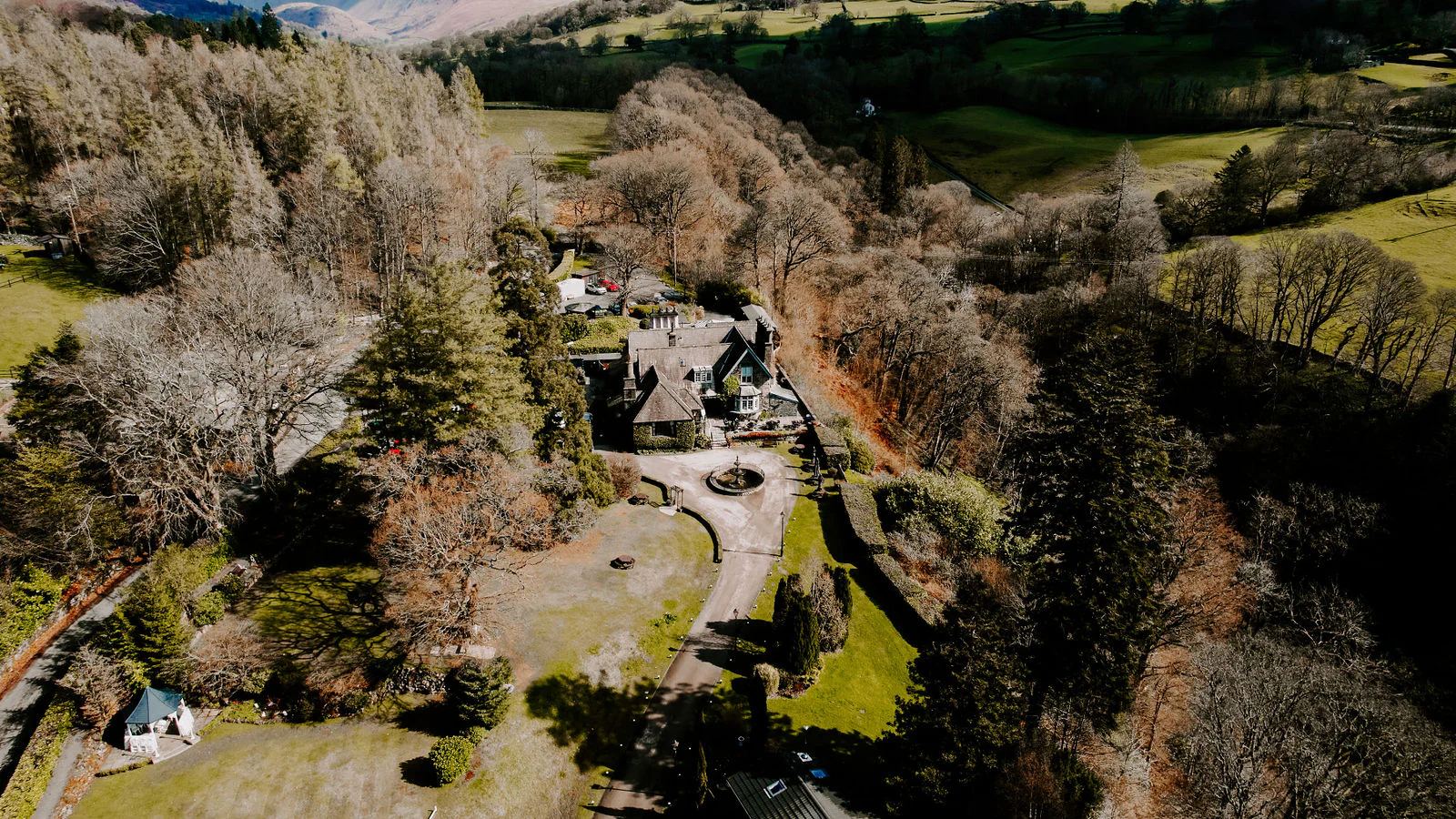 An aerial view of a stone house among trees and green hills near Windermere