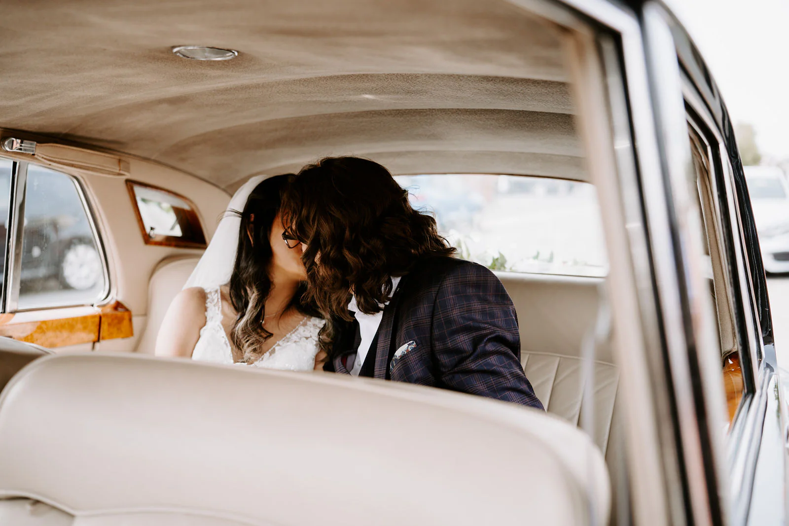 Anthony and Jasmine kiss in the back seat of a cream vintage car