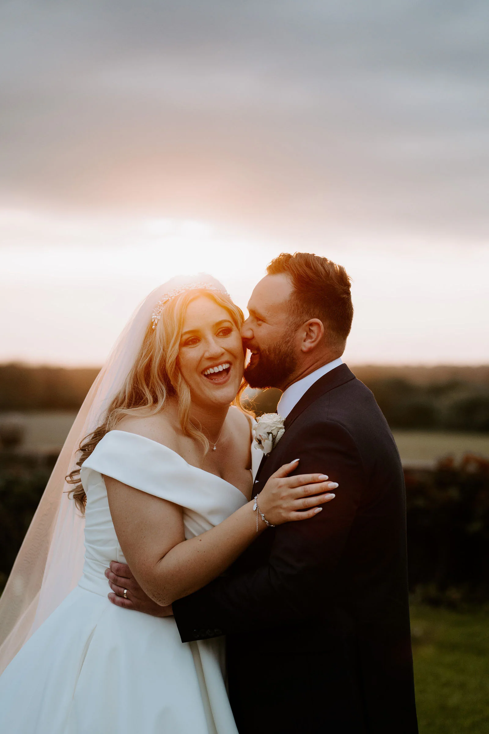 Emma laughing in an embrace with Sean in warm evening light during their sunset portraits