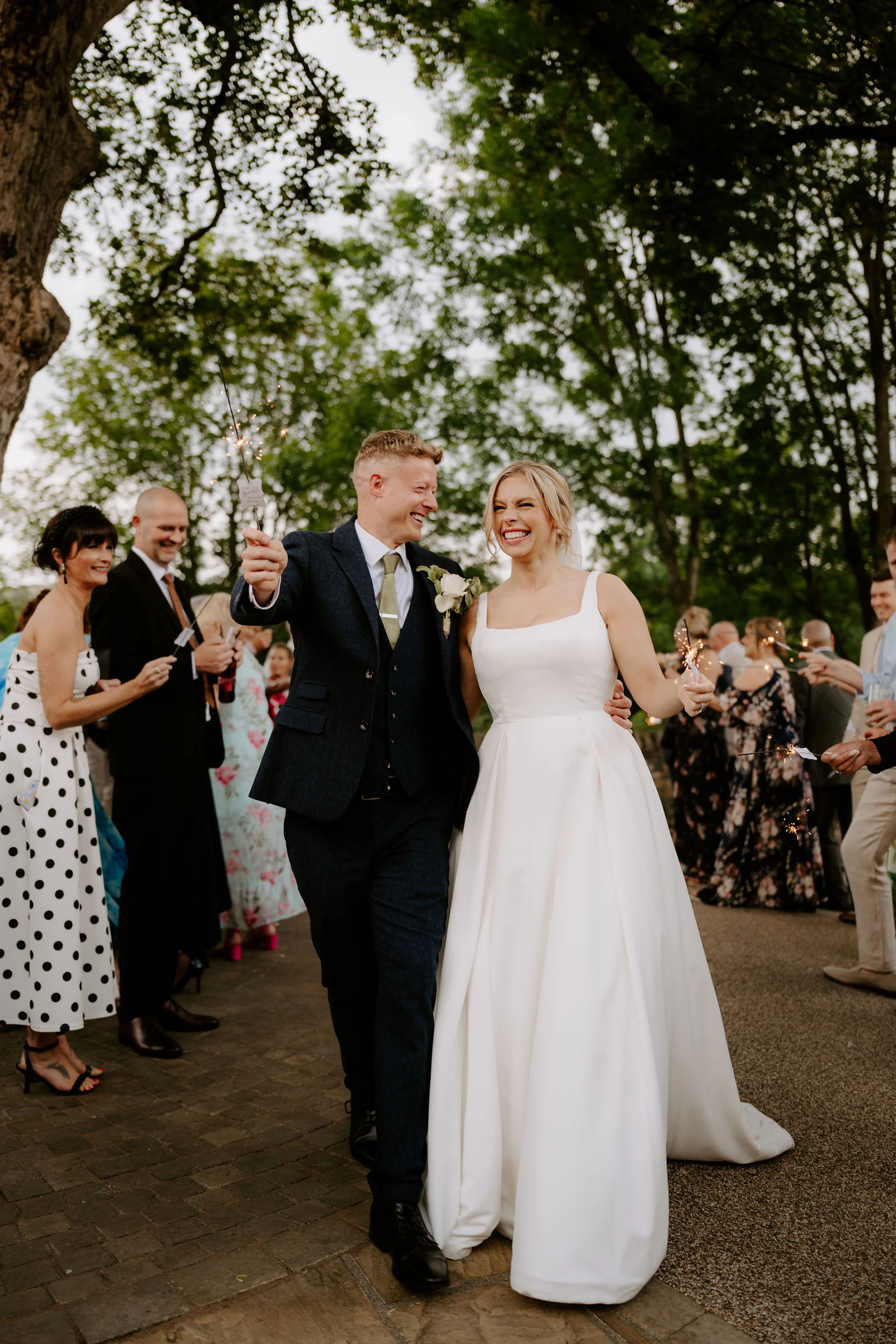 Amber and Will walking smiling beside guests who clap on a sunny path