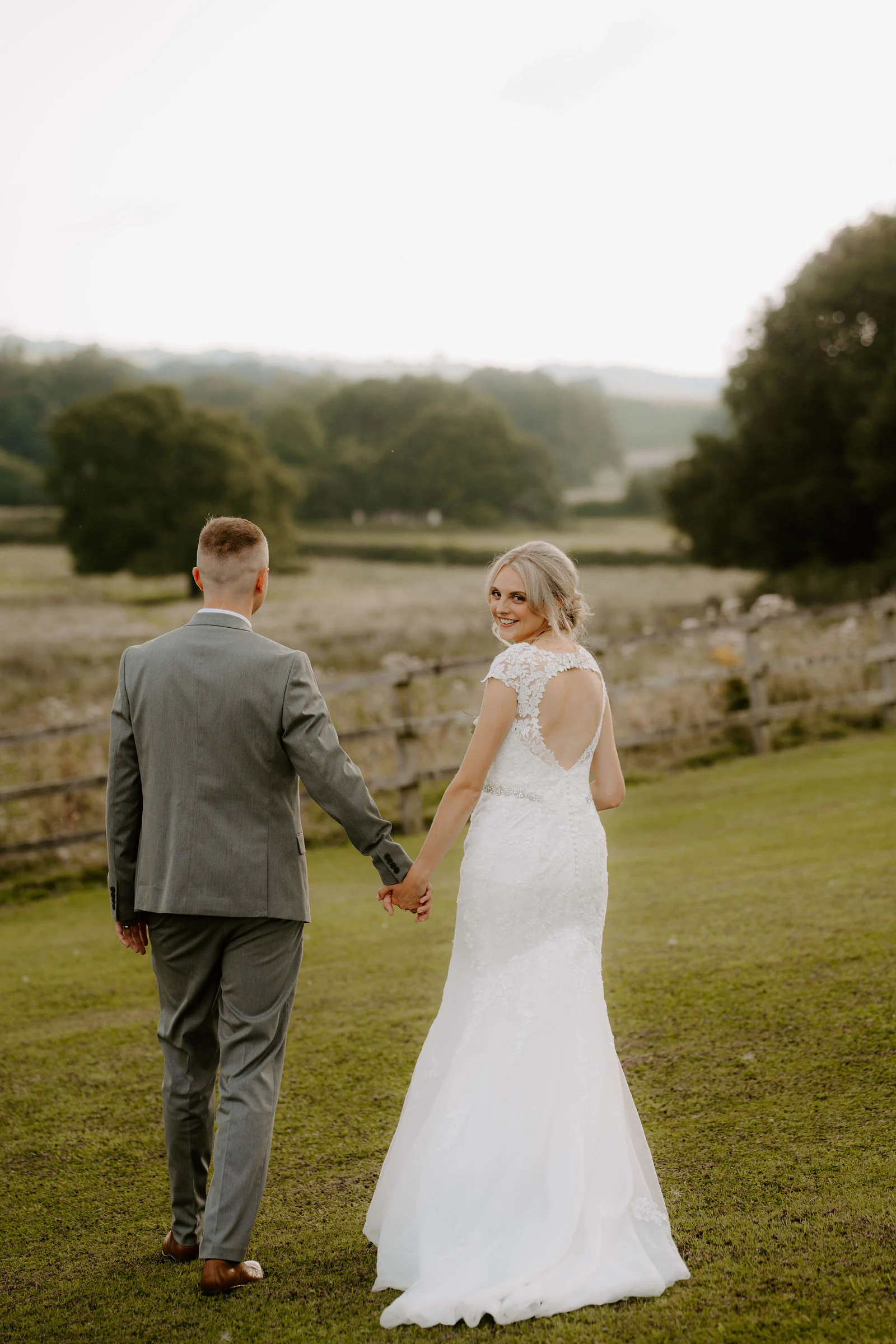 Brittany and Callum walking hand in hand across a lawn towards open fields as Brittany looks back