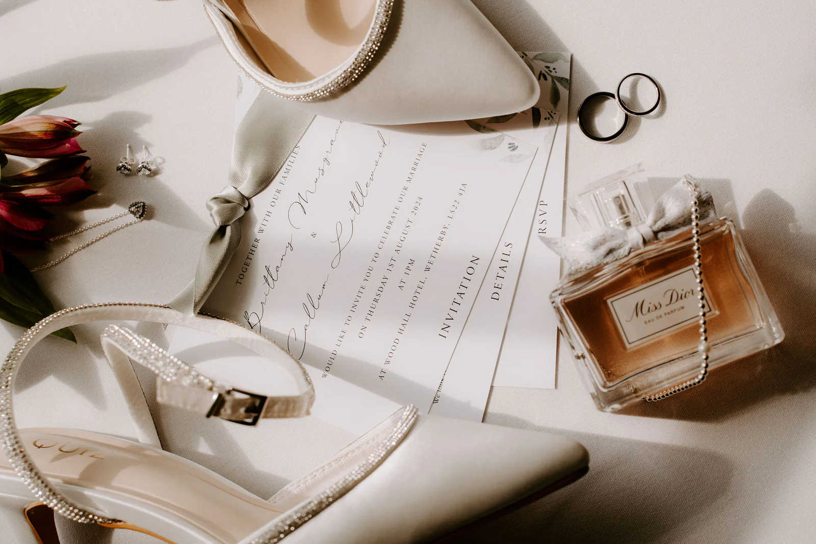 A wedding invitation laid out with bridal shoes, rings and perfume