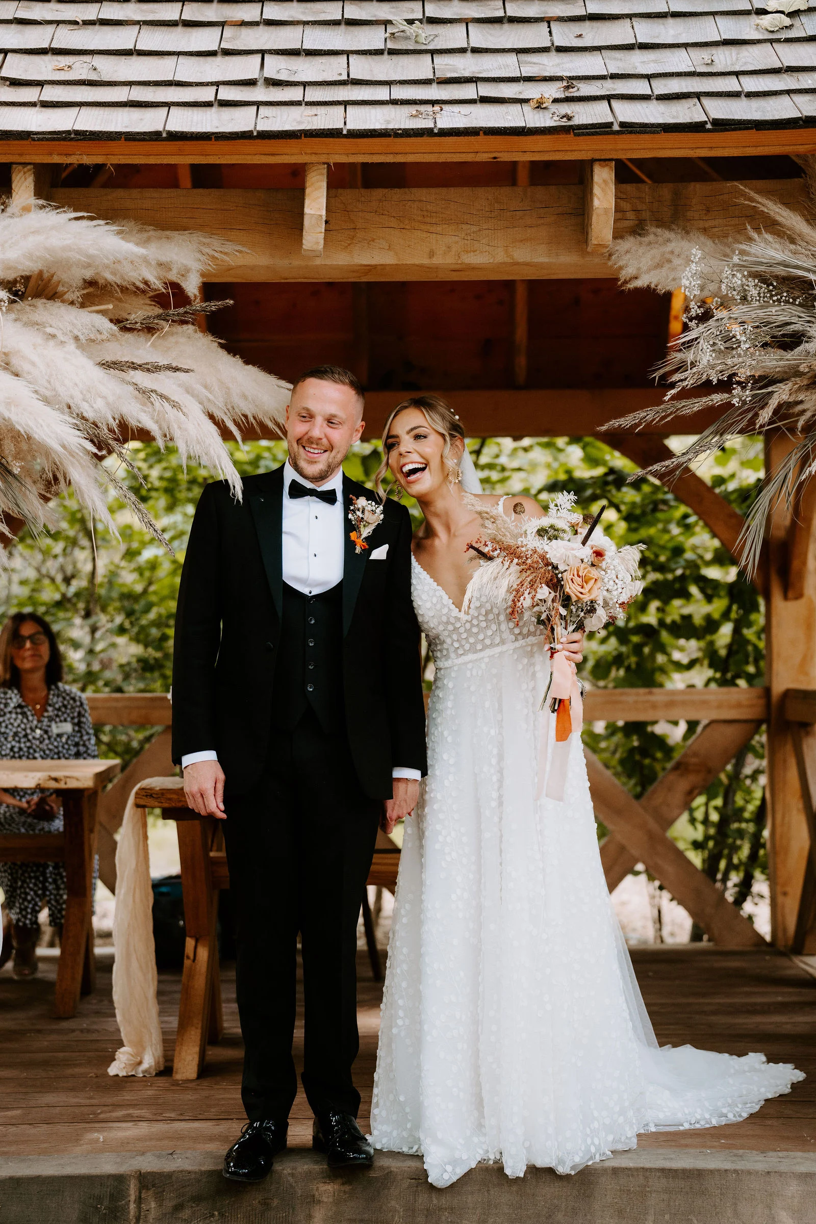 Emma and Tom smiling together beside a timber building at Hothorpe