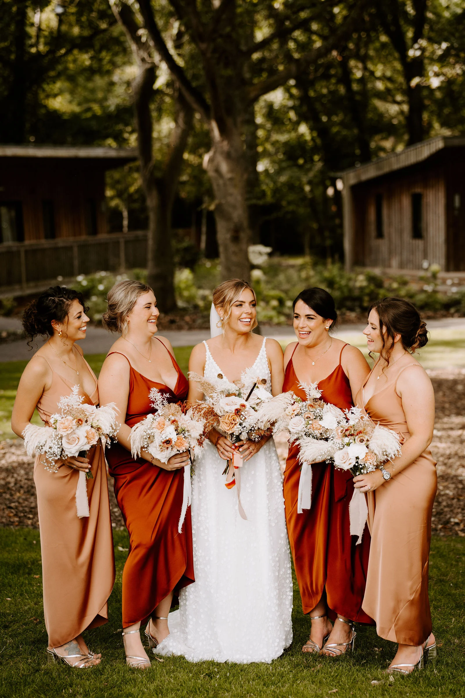 Emma standing with her wedding party and their bouquets beneath the trees