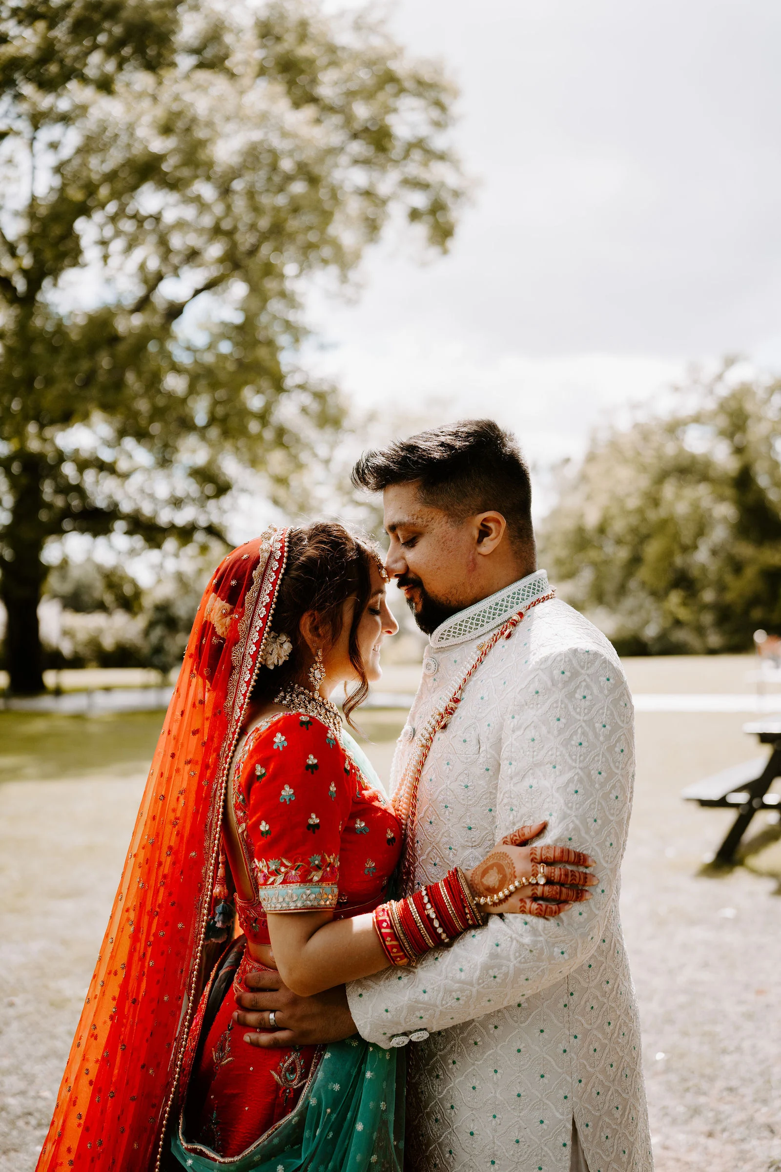 Nalini and Sanjay embracing outdoors against a leafy backdrop