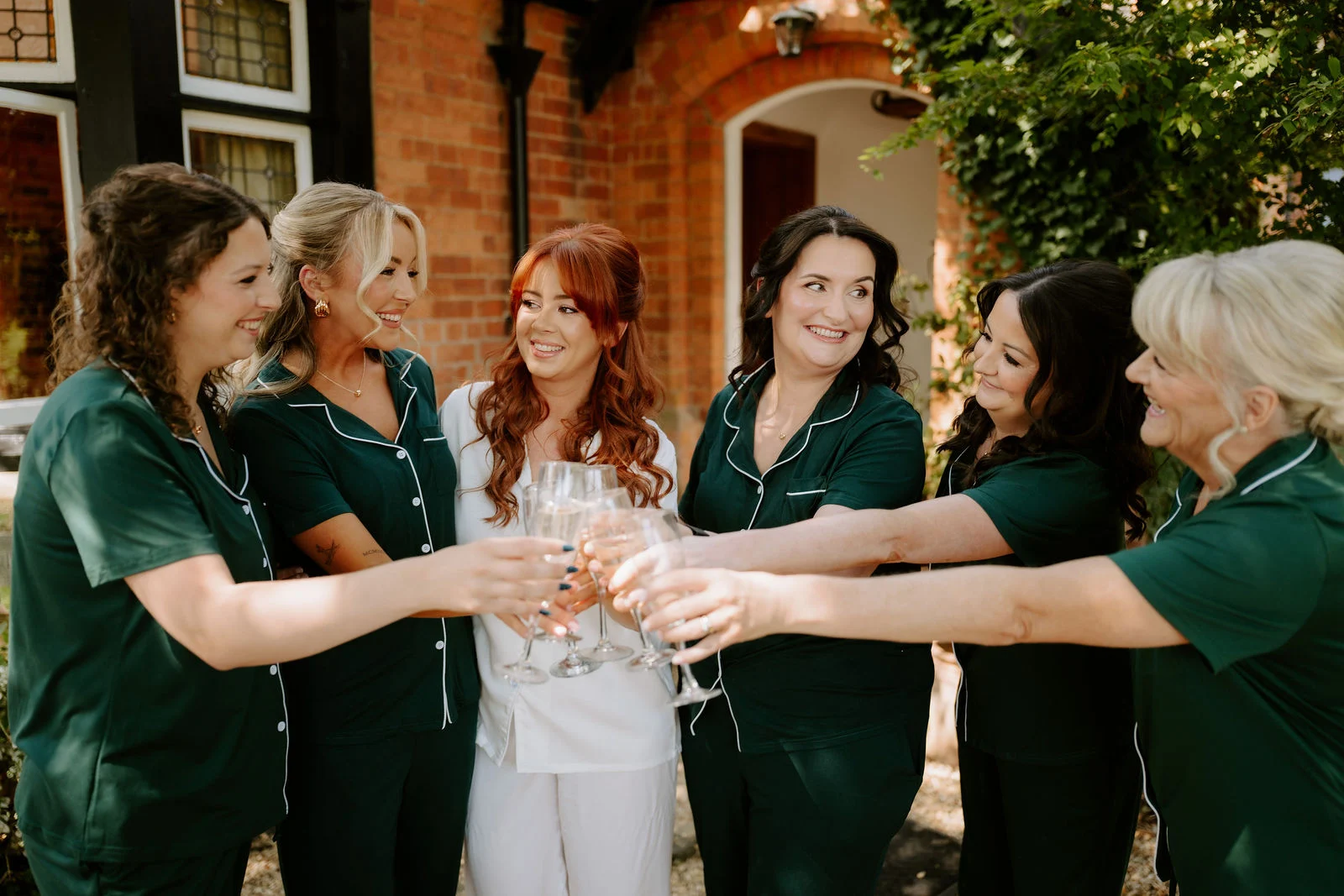 Amee raising a glass with her wedding party outside the timber buildings at Hothorpe