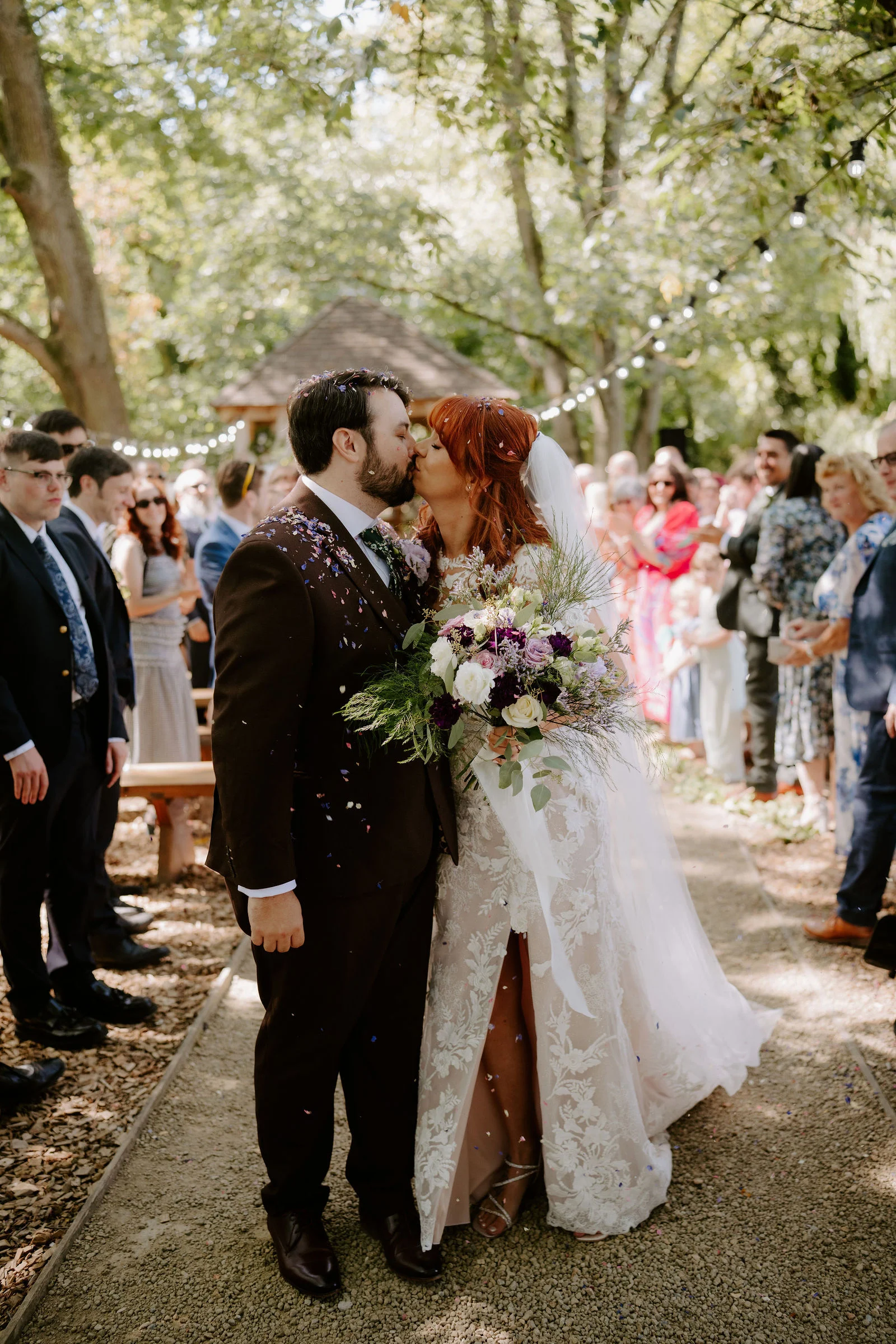 Amee and Sean kissing as guests look on in the woodland ceremony space