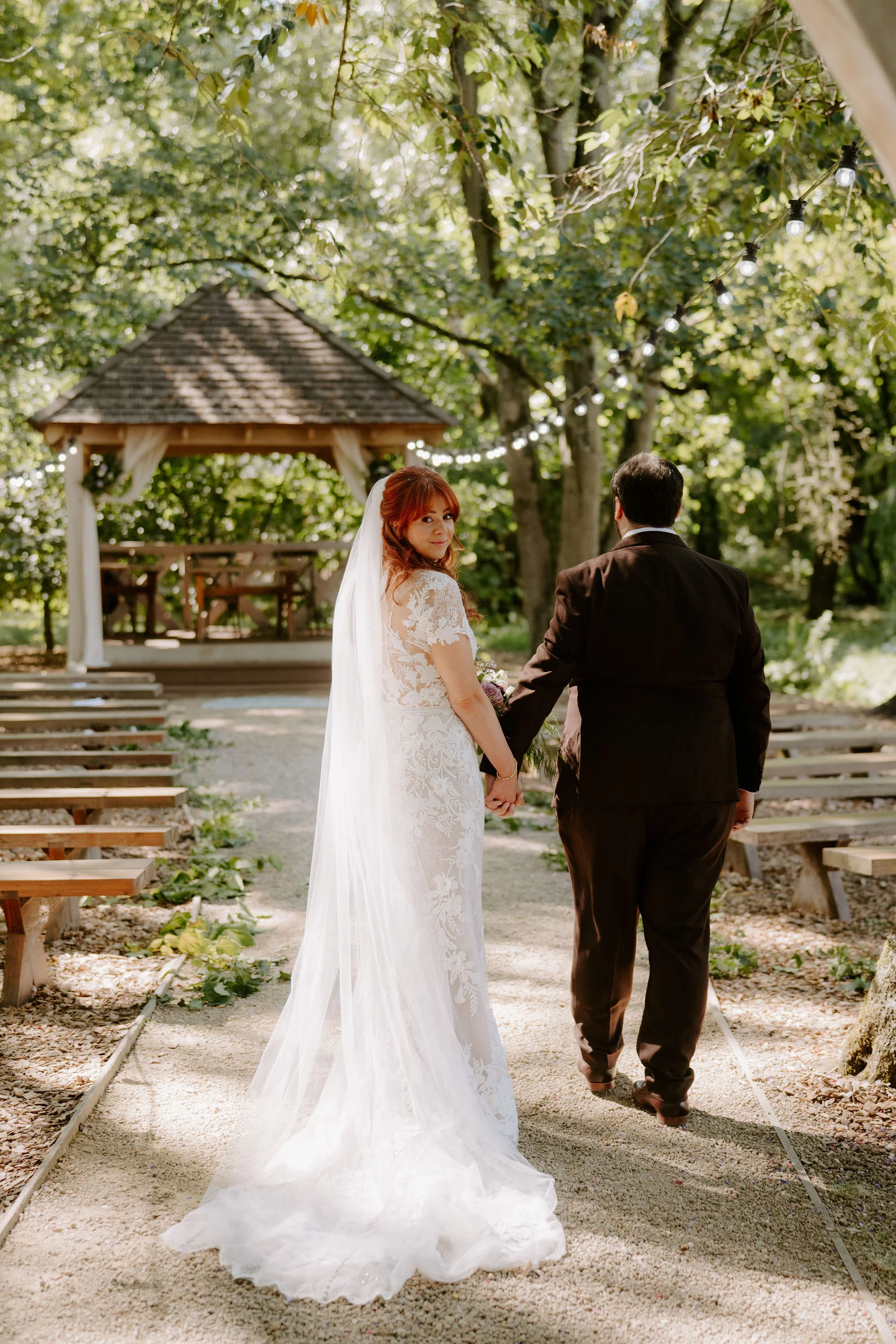 Amee and Sean walking hand in hand past the timber pavilion at Hothorpe