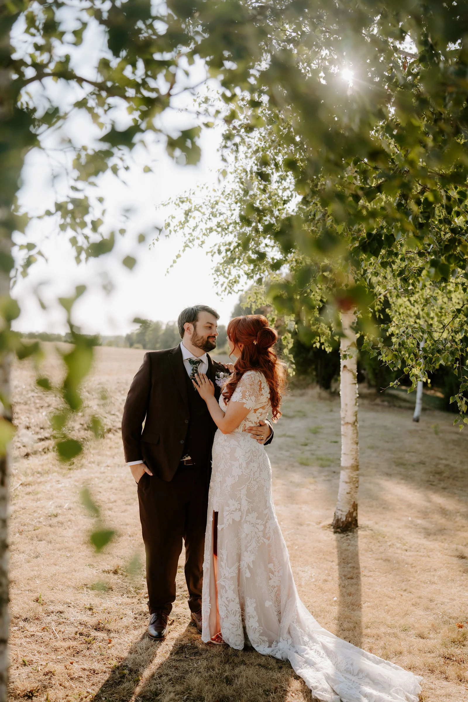 Amee and Sean embracing on a tree-lined path in warm light