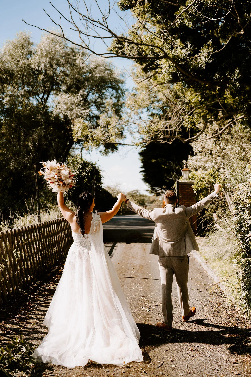 Hannah and Tom raising their arms on a tree-lined path after their ceremony