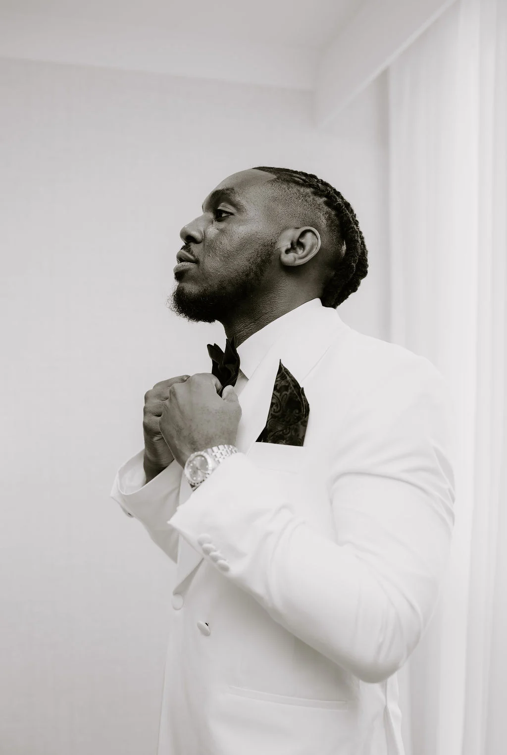 Tobenna adjusting his tie in a black and white preparation photograph.