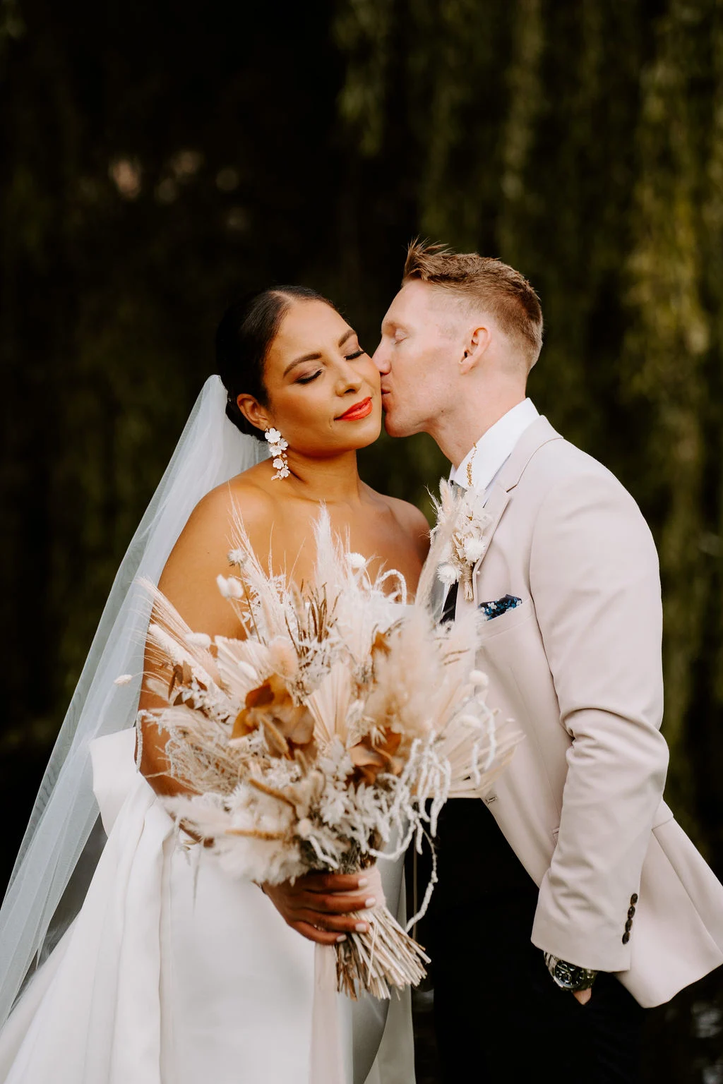 Shanice and Russel kissing with her bouquet between them.