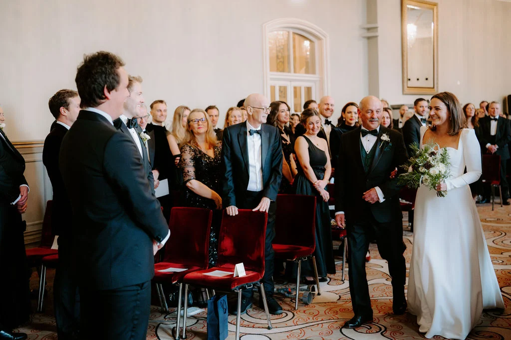 Jo and Sam during their ceremony with guests beside the windows.
