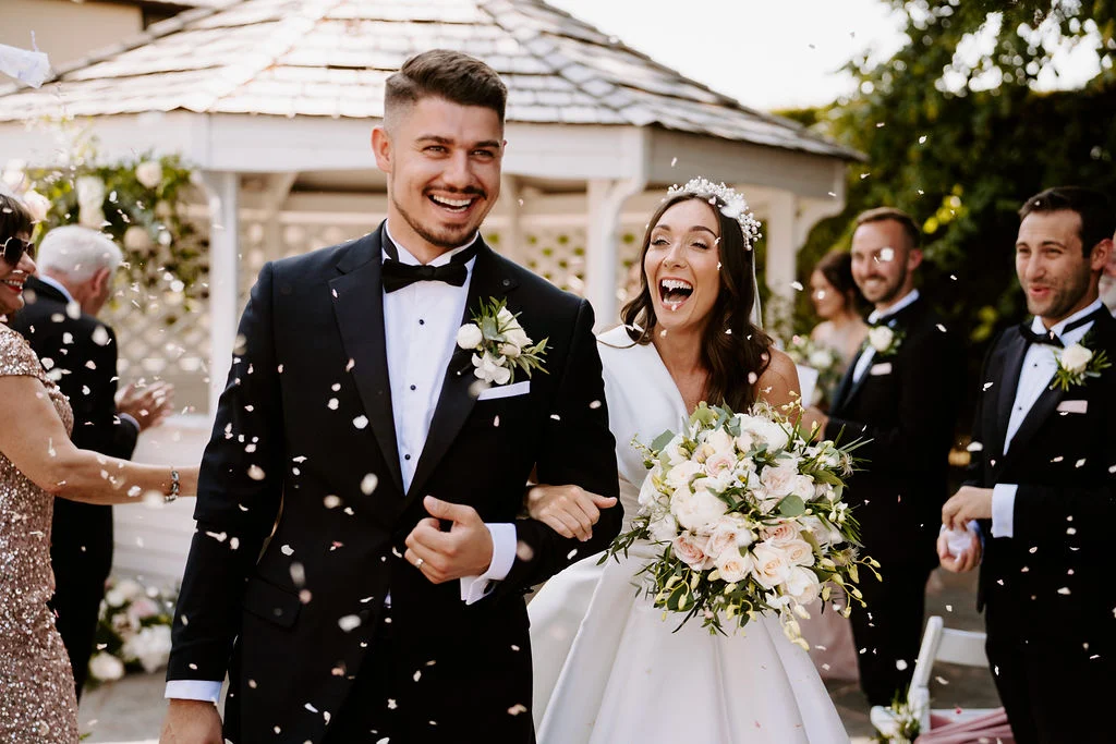 Natalie and Damian smiling through confetti after their ceremony at West Tower