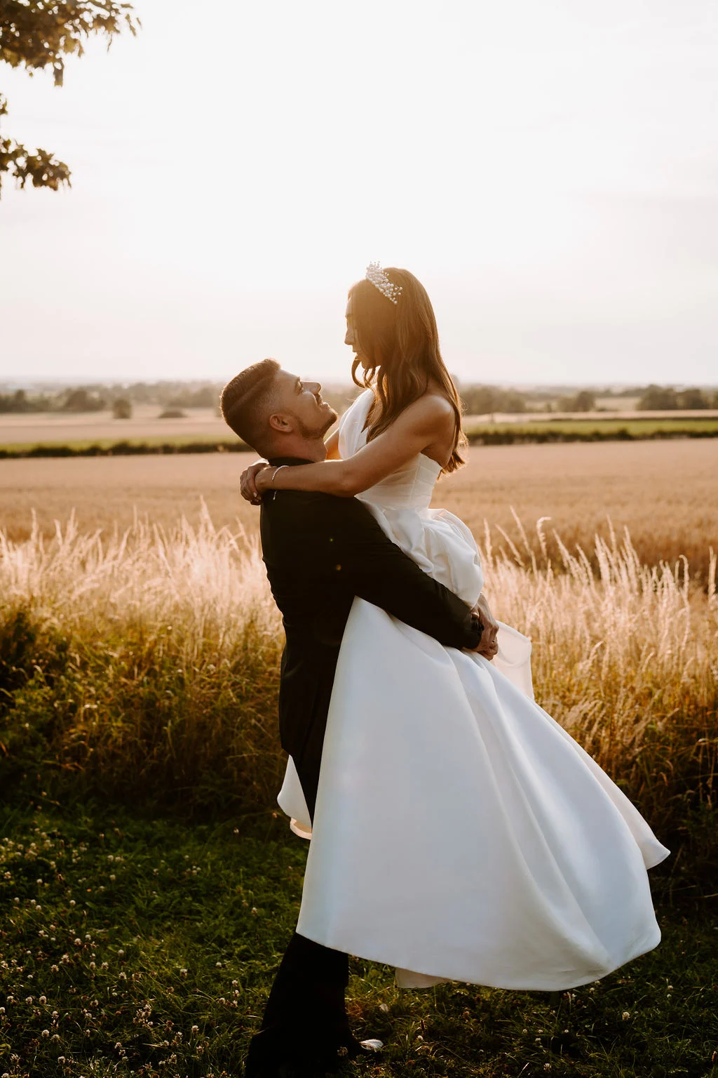 Damian lifting Natalie in a joyful moment beside the fields