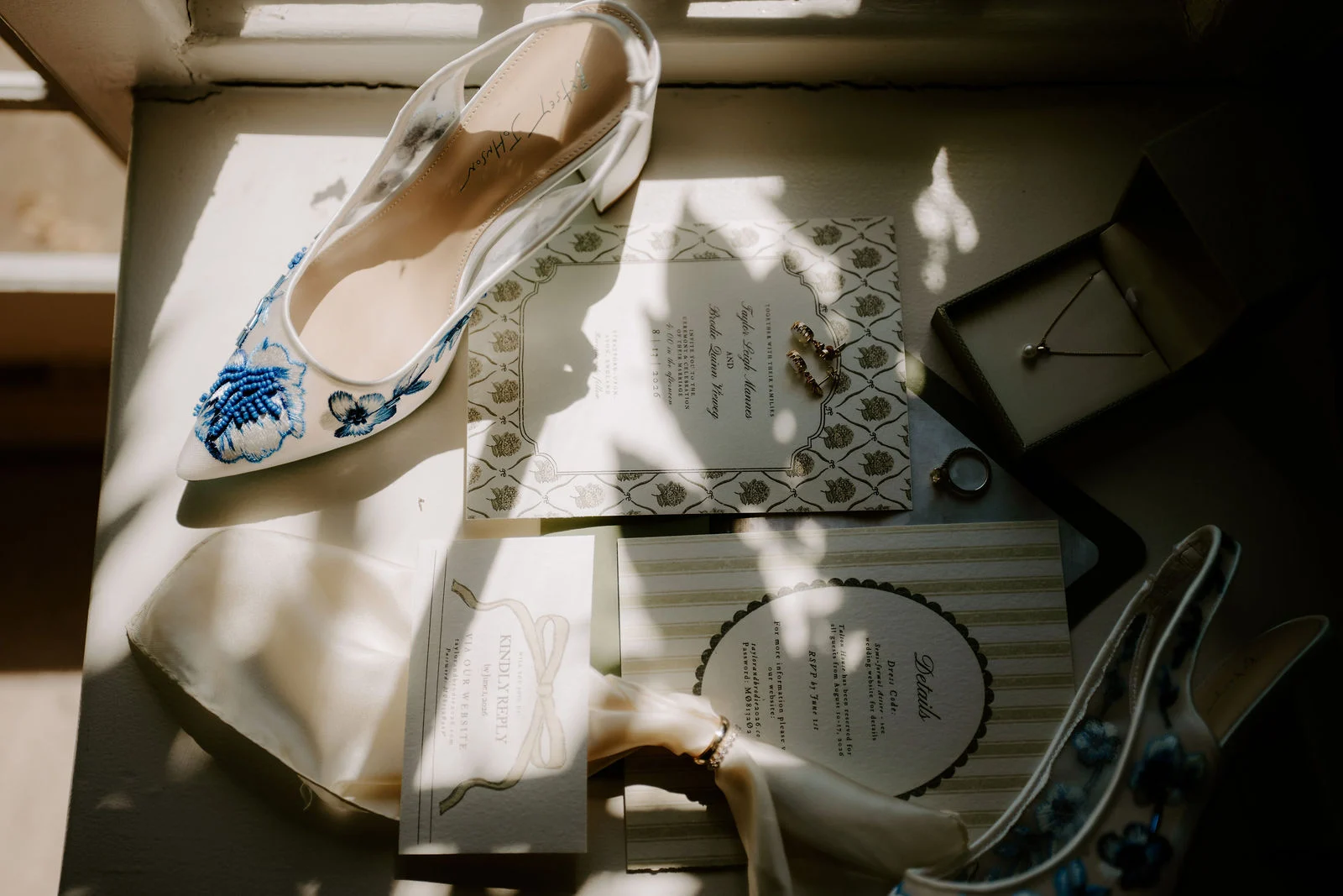 Embroidered white shoes, letterpress stationery, a jewellery box and small gold pieces are laid out on a windowsill in dappled sunlight.