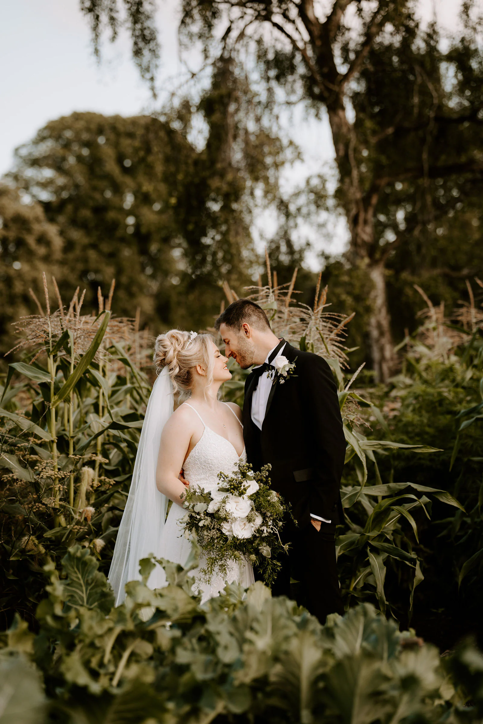 A bride and groom embrace among tall grasses and flowers in a garden