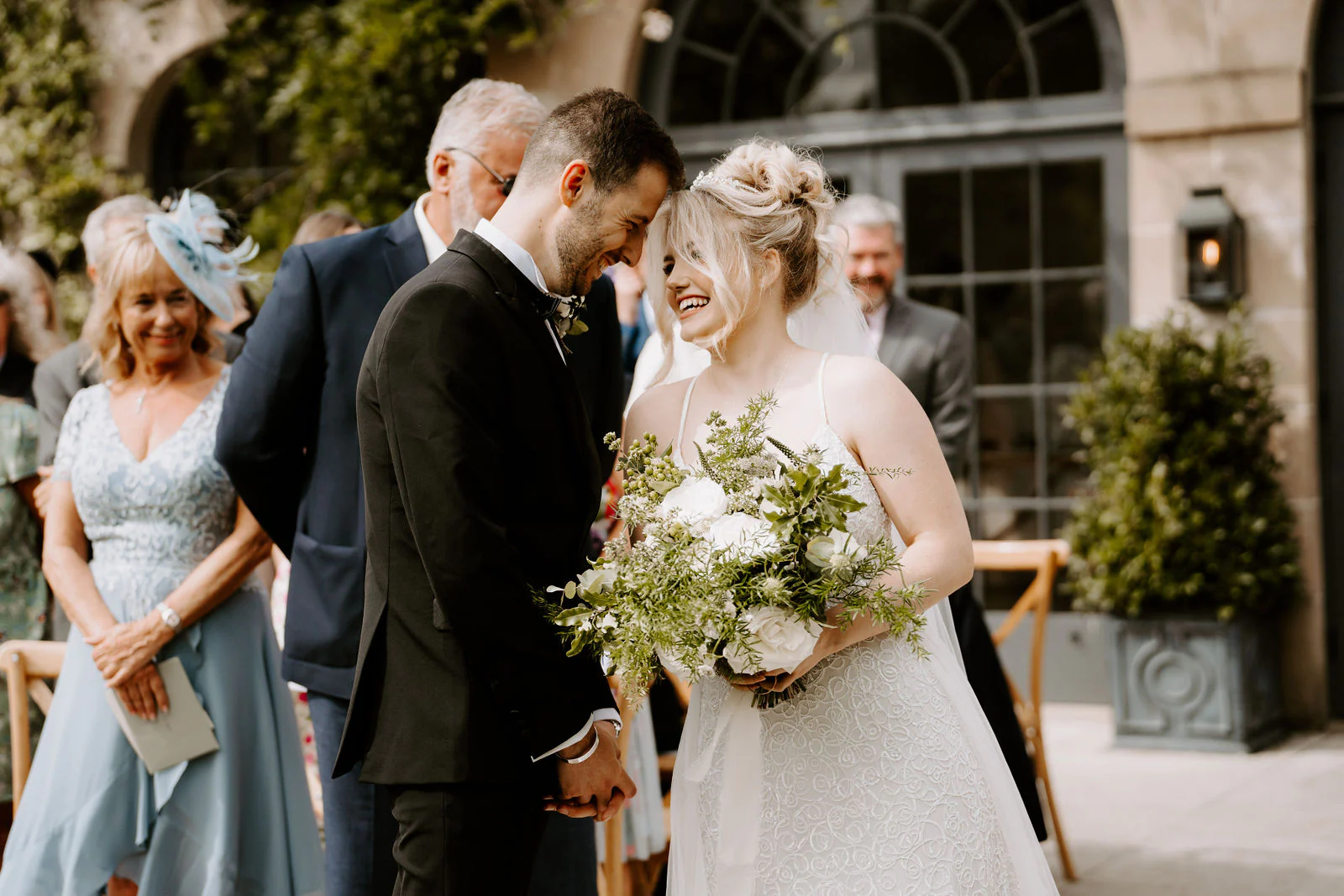 A groom and bride laugh with their foreheads together while guests look on during the ceremony