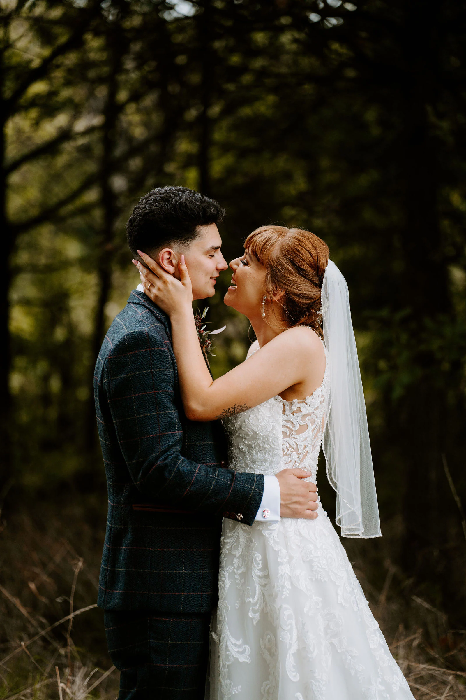 A bride and groom hold each other close among dark trees