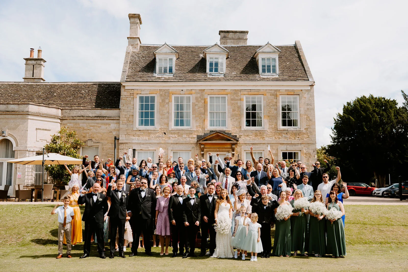 Laura and Gavin with their wedding guests in front of the historic house at Barton Hall