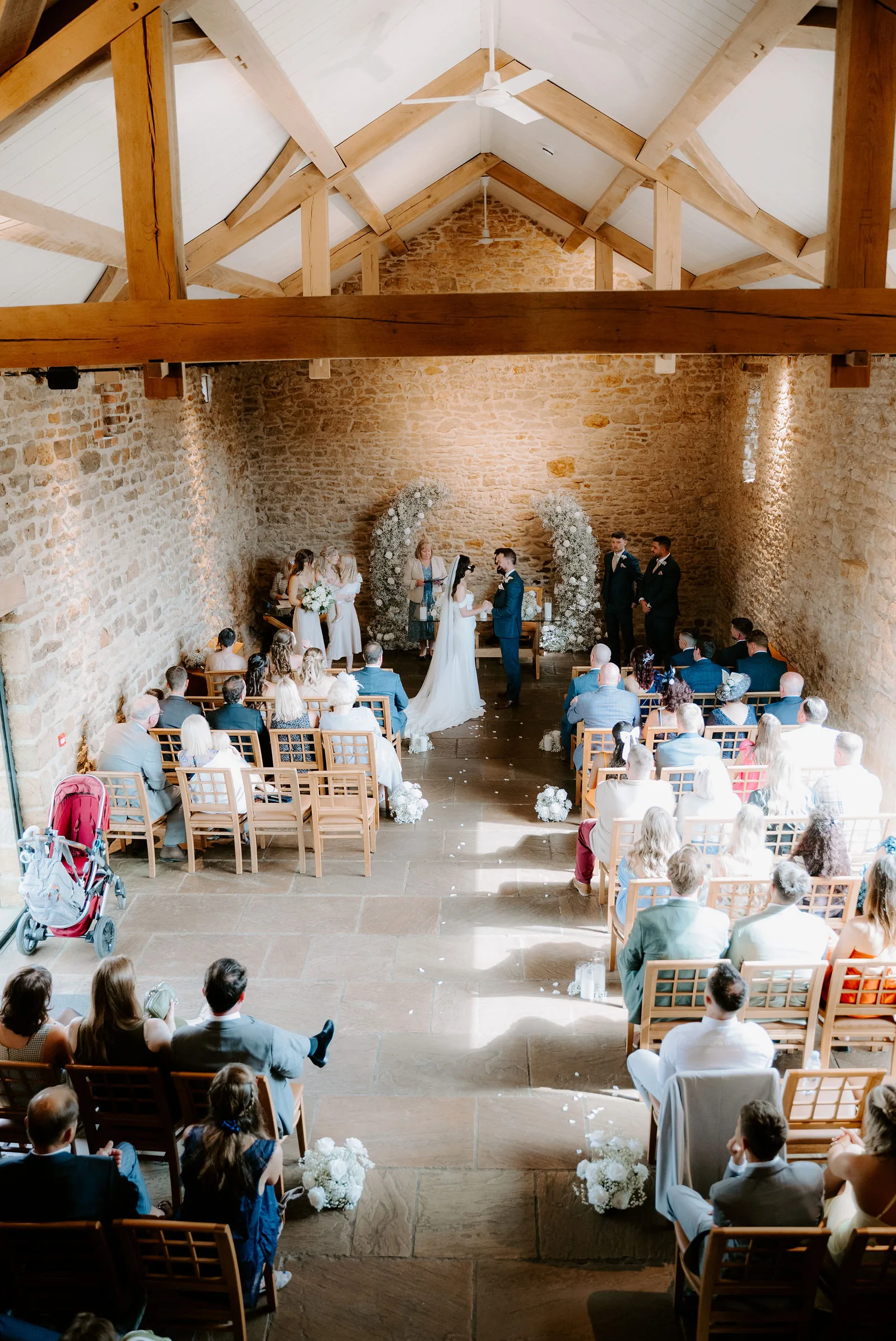 Charlie and Faye walking hand-in-hand outside the historic ironstone barns of Dodford Manor