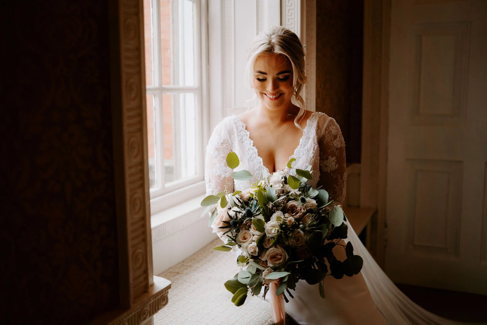 Charlotte holding her bouquet beside a tall window at Colwick Hall