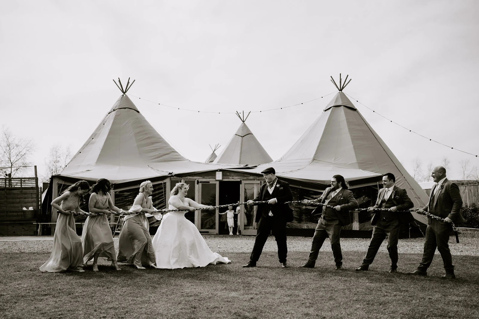 Becky and Rob pulling on opposite sides of a rope with guests in front of the wedding tipis