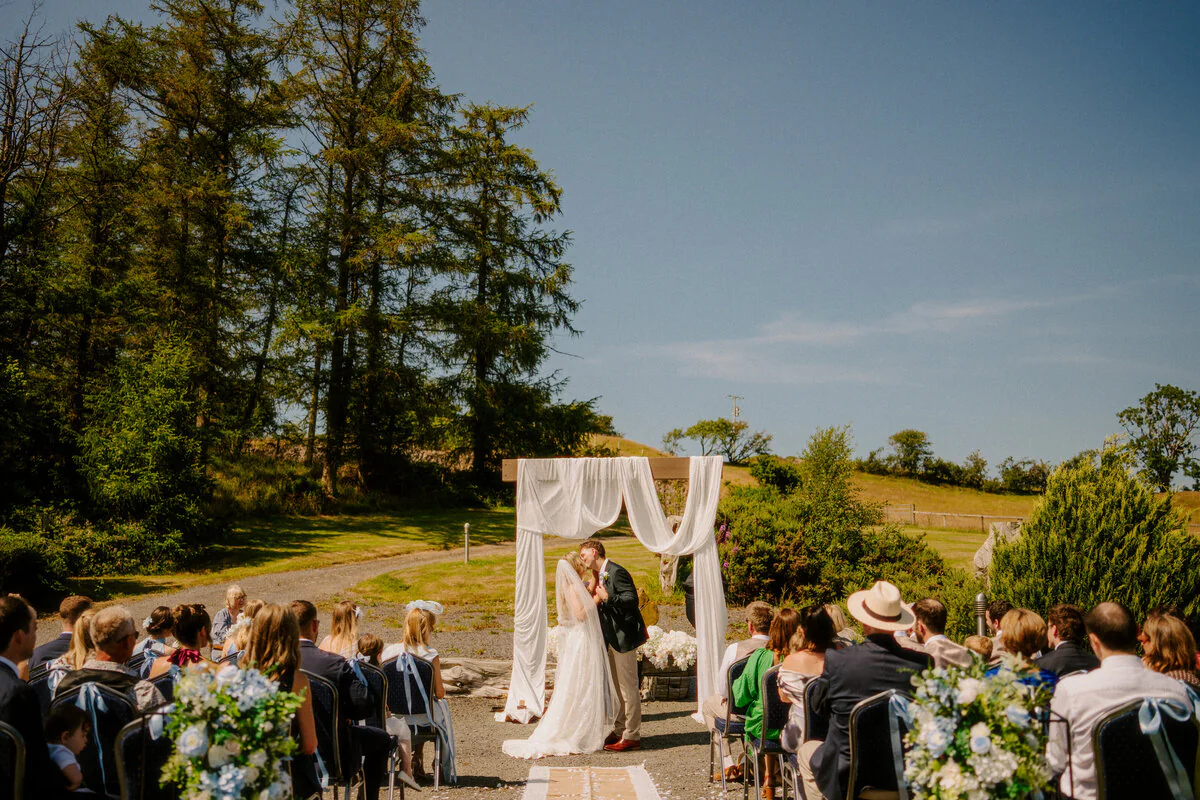 Outdoor wedding ceremony beneath tall trees, captured by a South Wales wedding photographer.