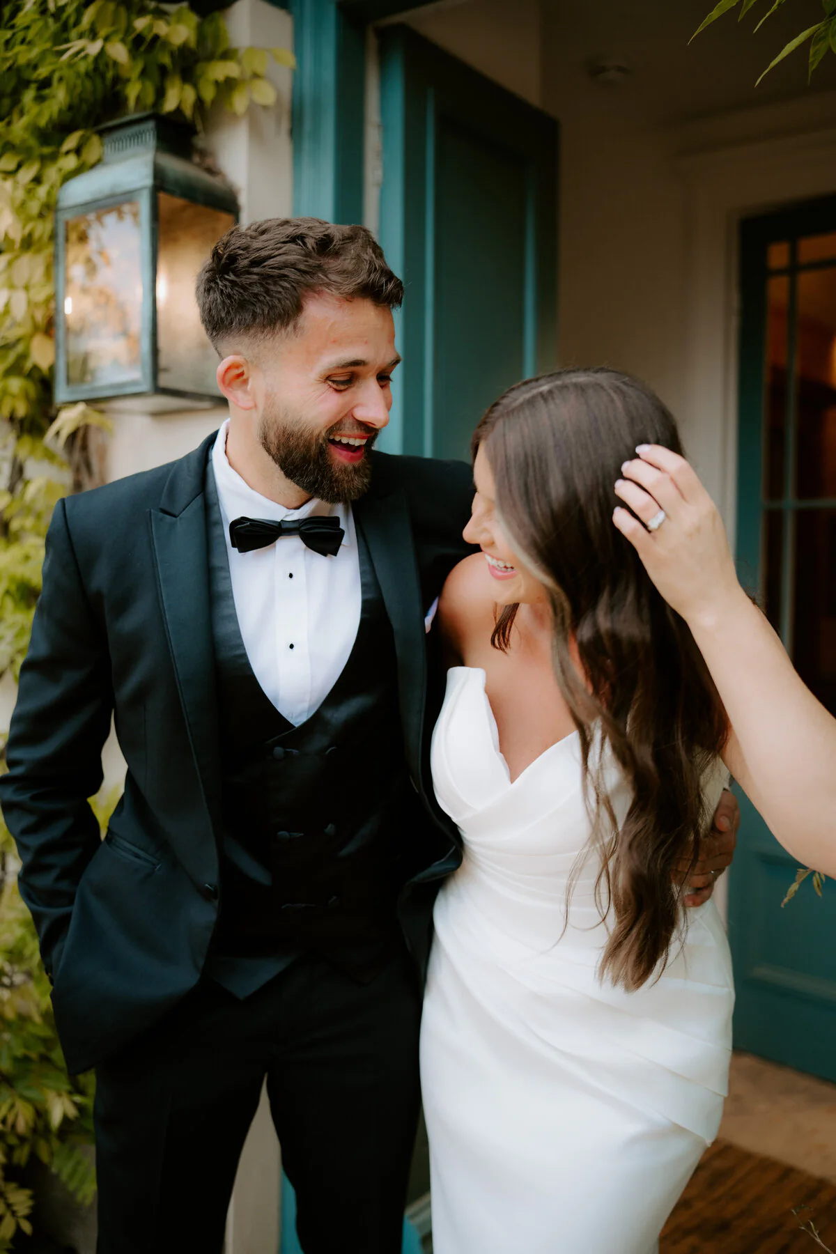 Bride in a strapless gown and groom in a tuxedo beside a lantern-lit teal door.