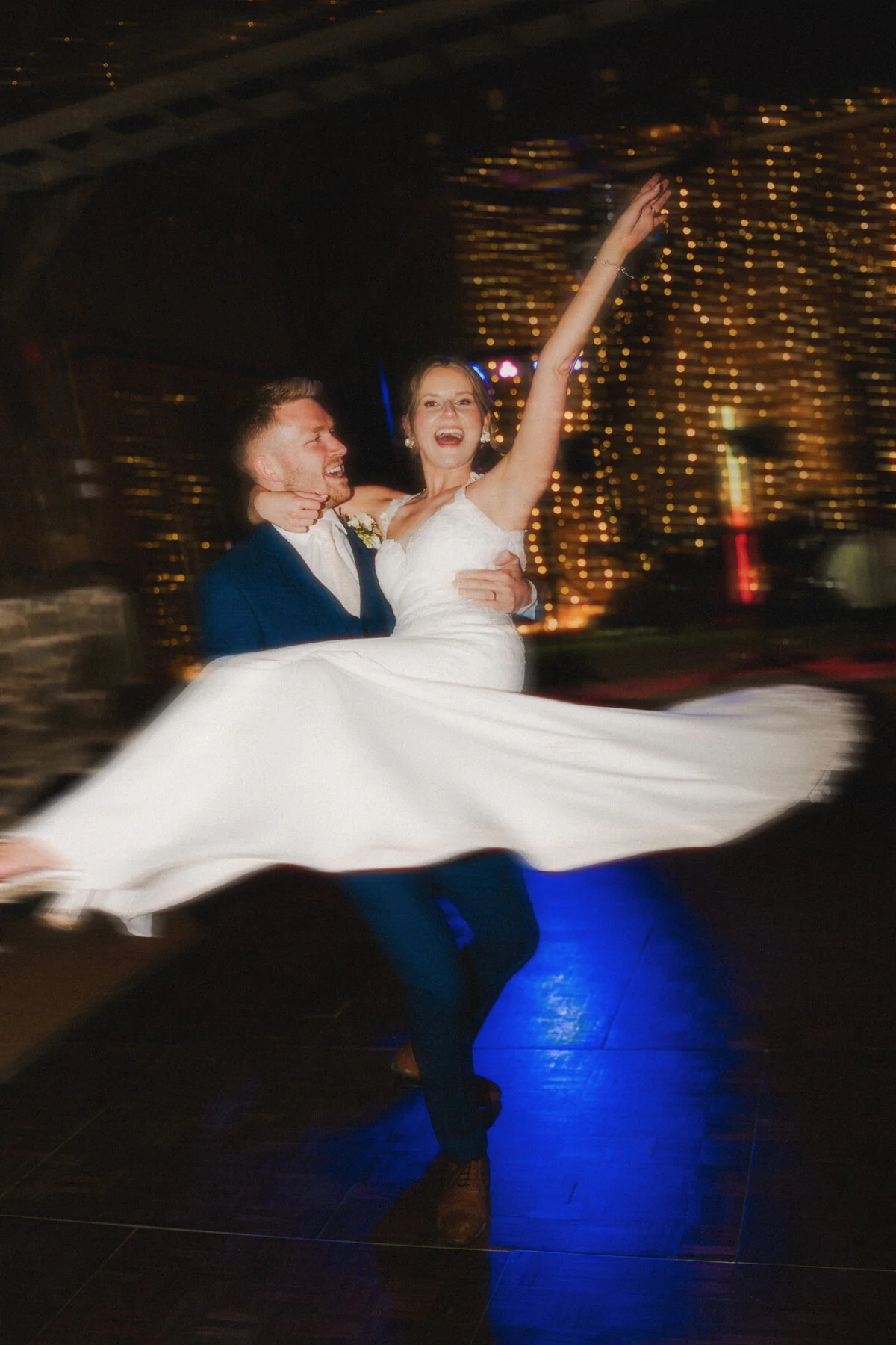 Groom lifting the bride while dancing at their evening wedding reception.