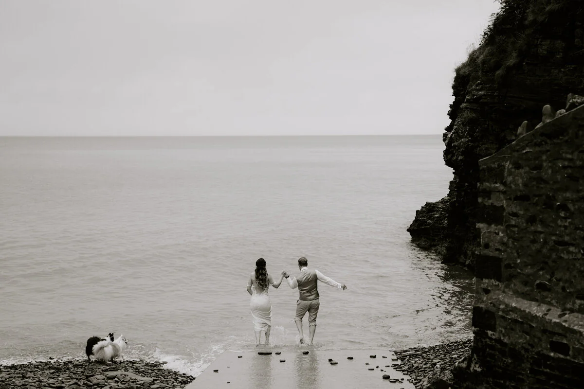 Black and white photograph of a couple walking together along a rocky coastline.