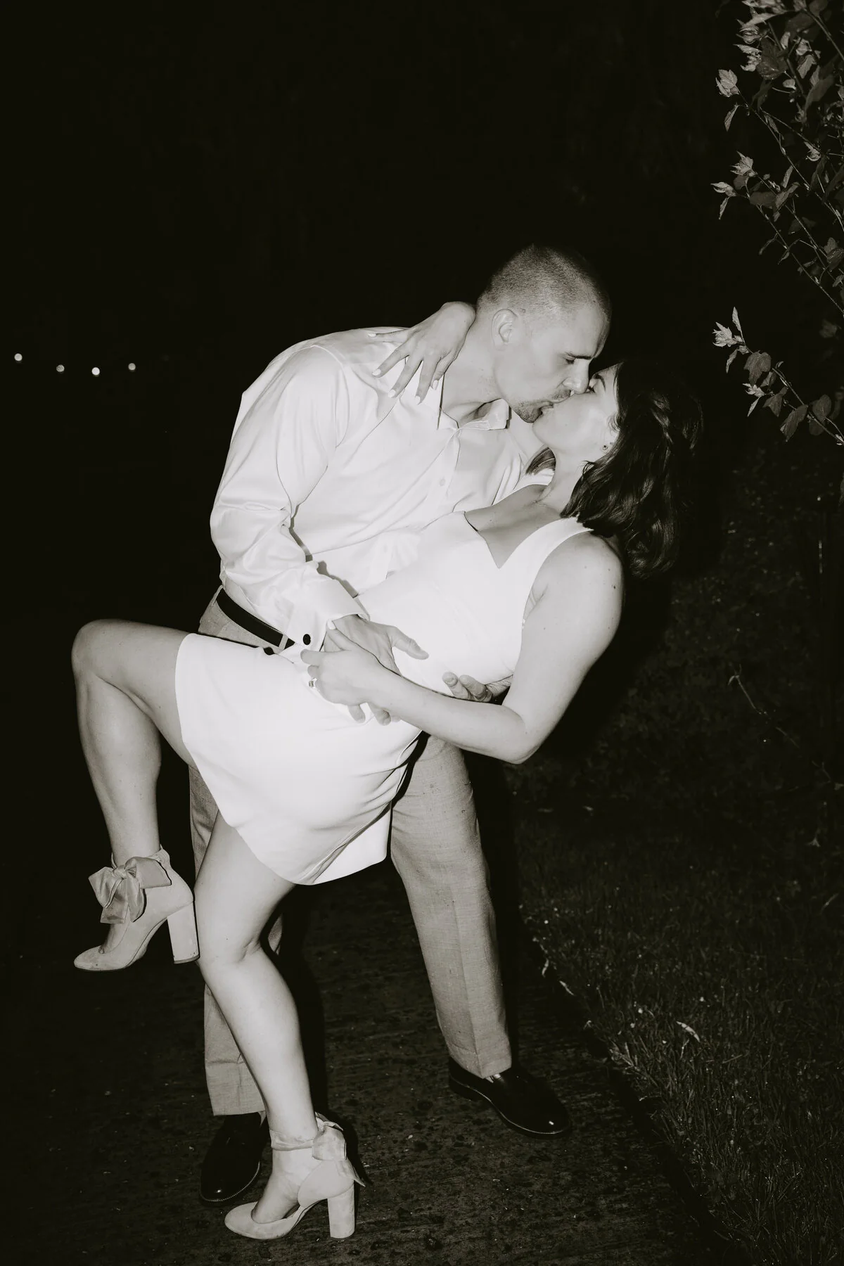 Black and white flash photograph of a couple kissing during an evening dip in a short white dress.