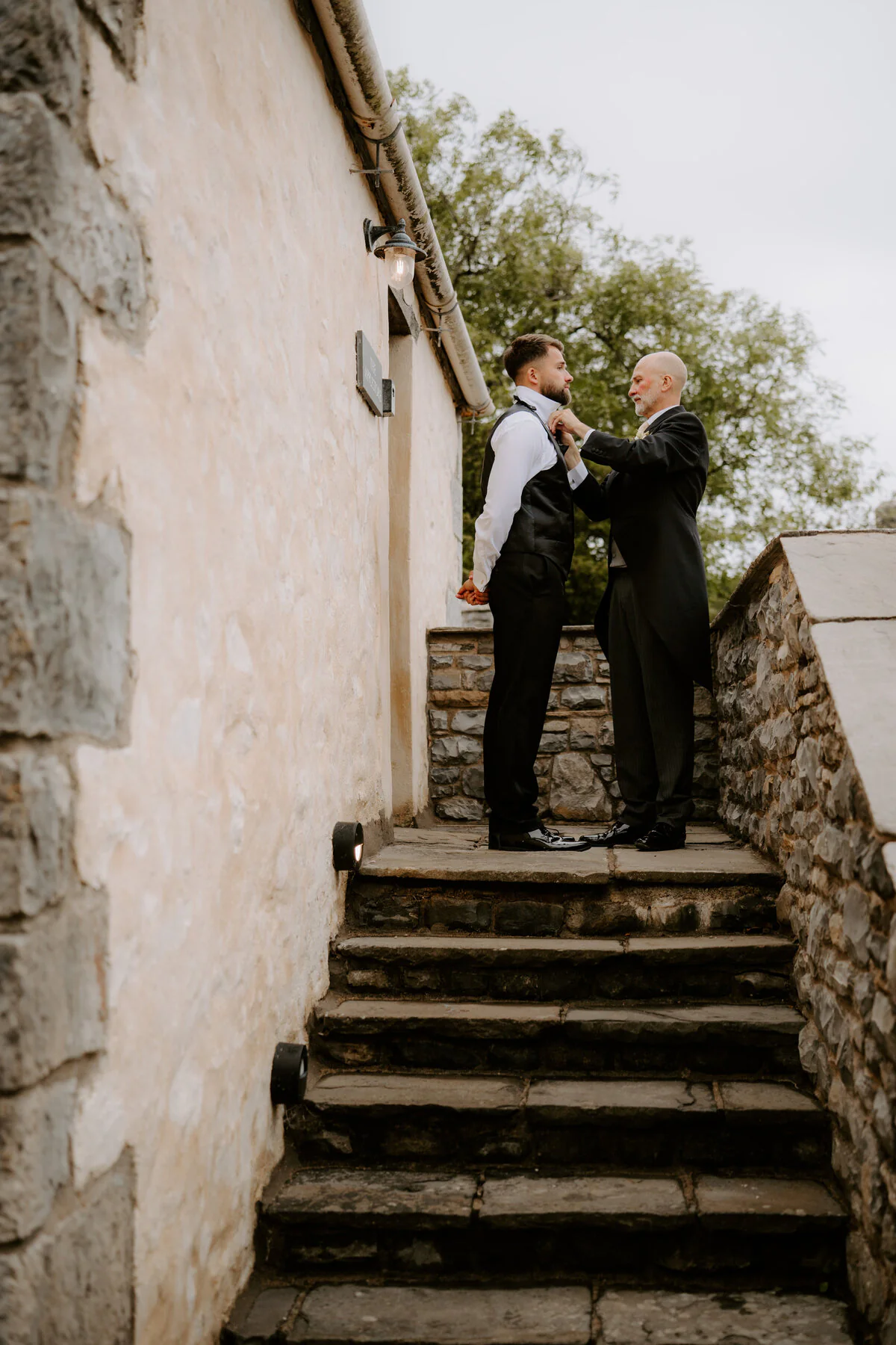 Groom having his tie adjusted on stone steps before the wedding ceremony.