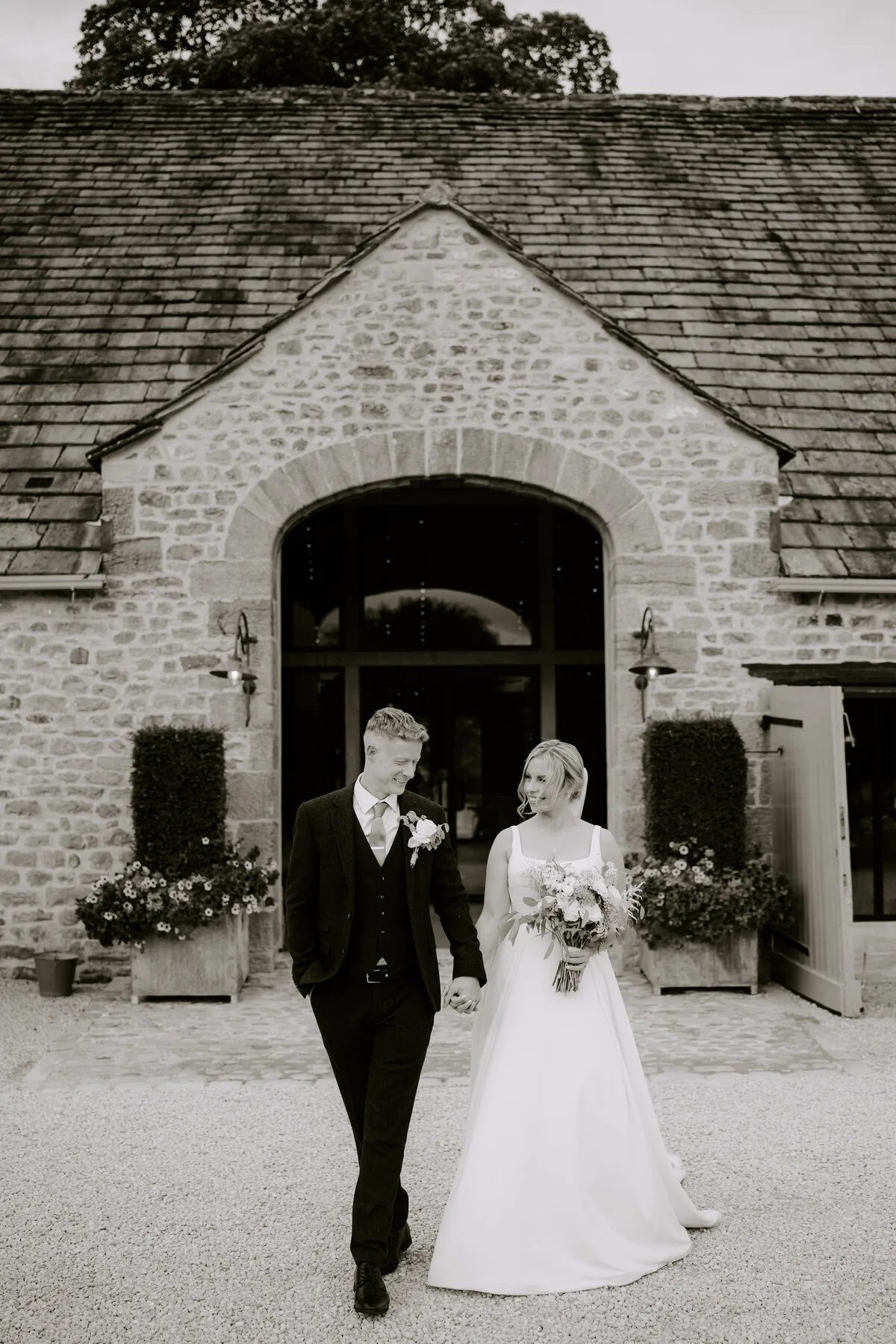 Black and white photograph of newlyweds walking outside a stone barn wedding venue.