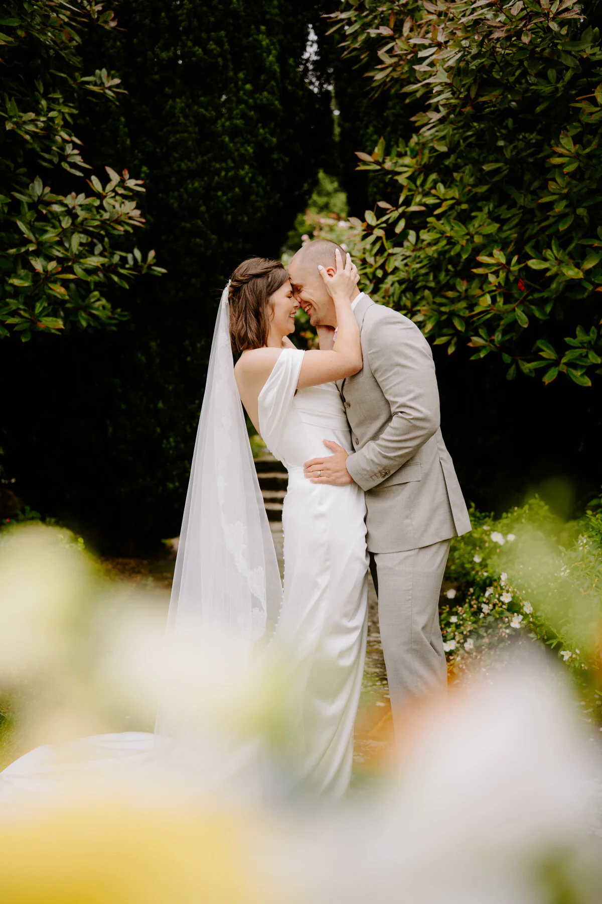 Bride and groom sharing a quiet kiss in a leafy wedding venue garden.