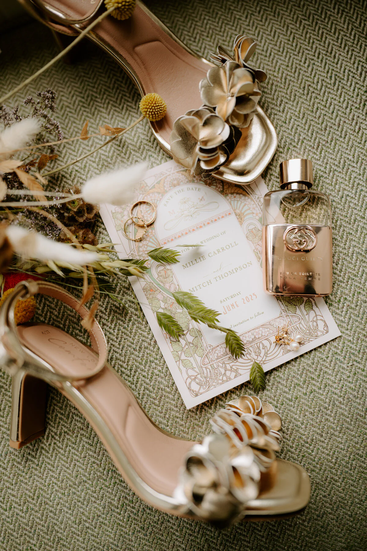 Wedding flat lay with gold heels, rings, perfume and Millie and Mitch's save-the-date card.