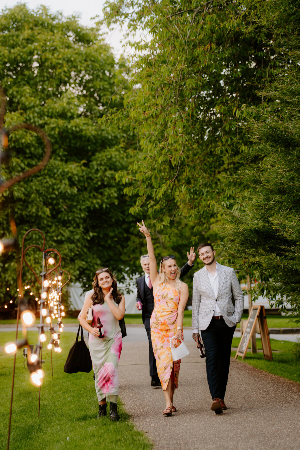 Wedding guests in colourful dresses walking a festoon-lit path in the evening.