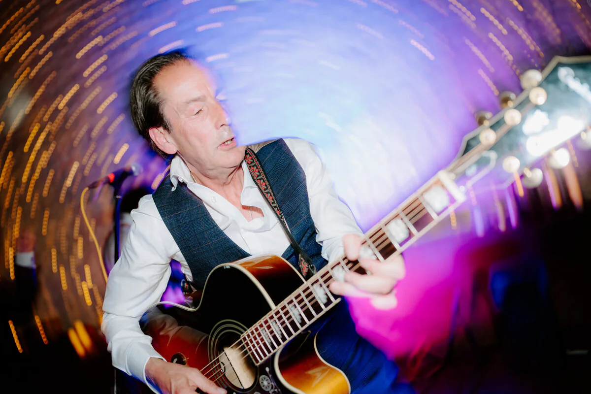 Wedding guitarist playing beneath swirling colourful dance-floor light trails.