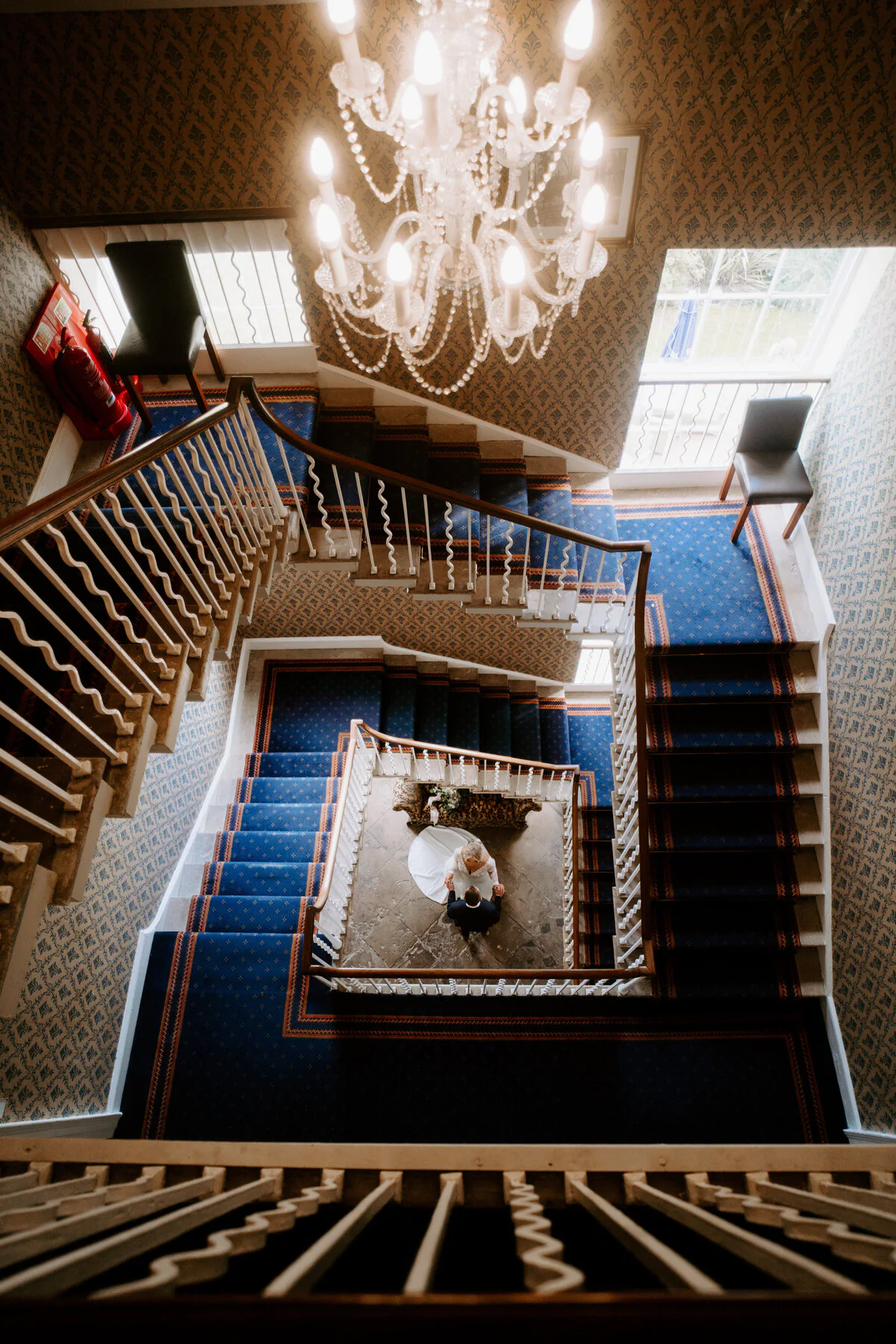 Overhead view of a grand spiral staircase with blue carpet and a chandelier.