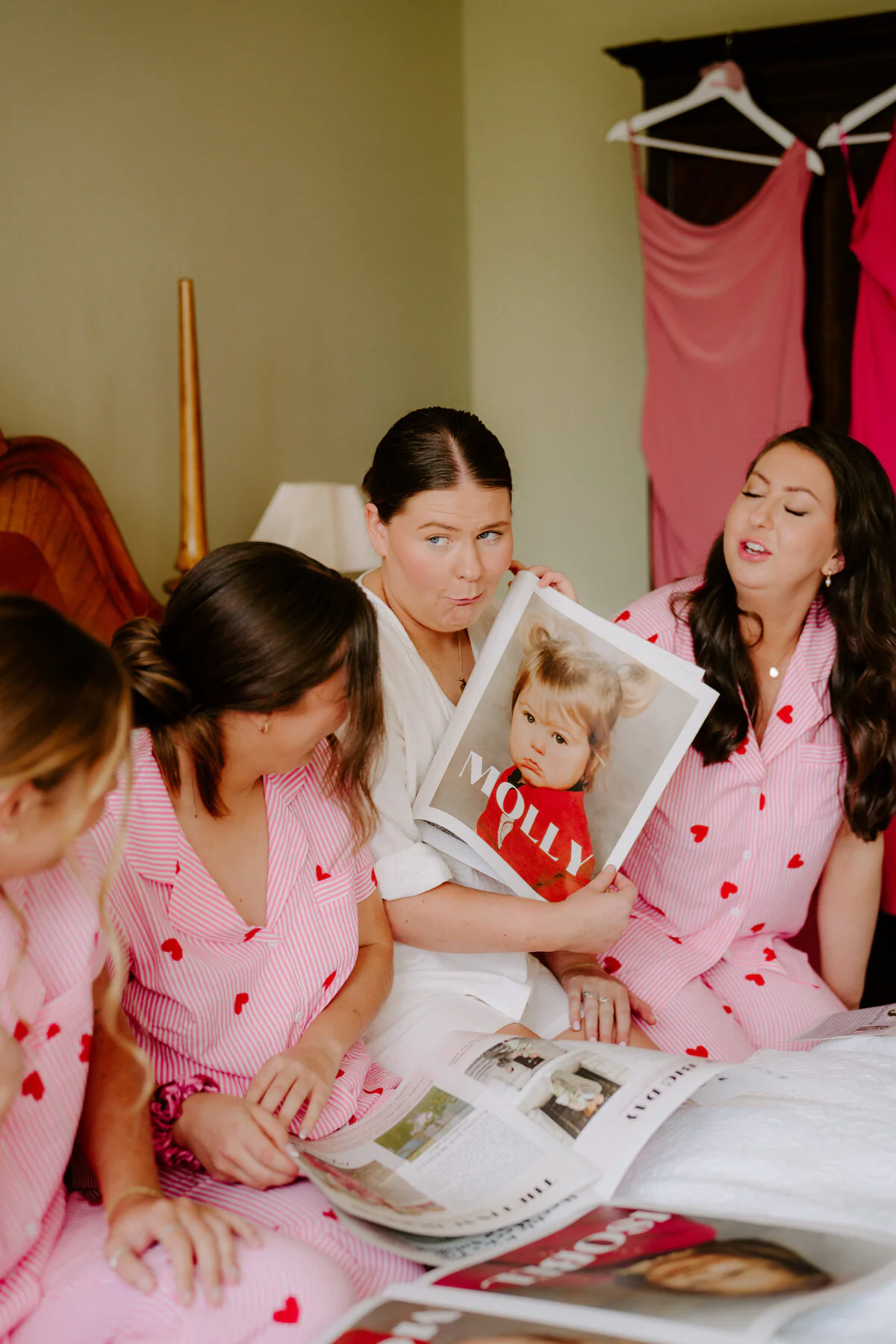 Bride and bridesmaids in pink heart pyjamas looking at a magazine during morning prep.