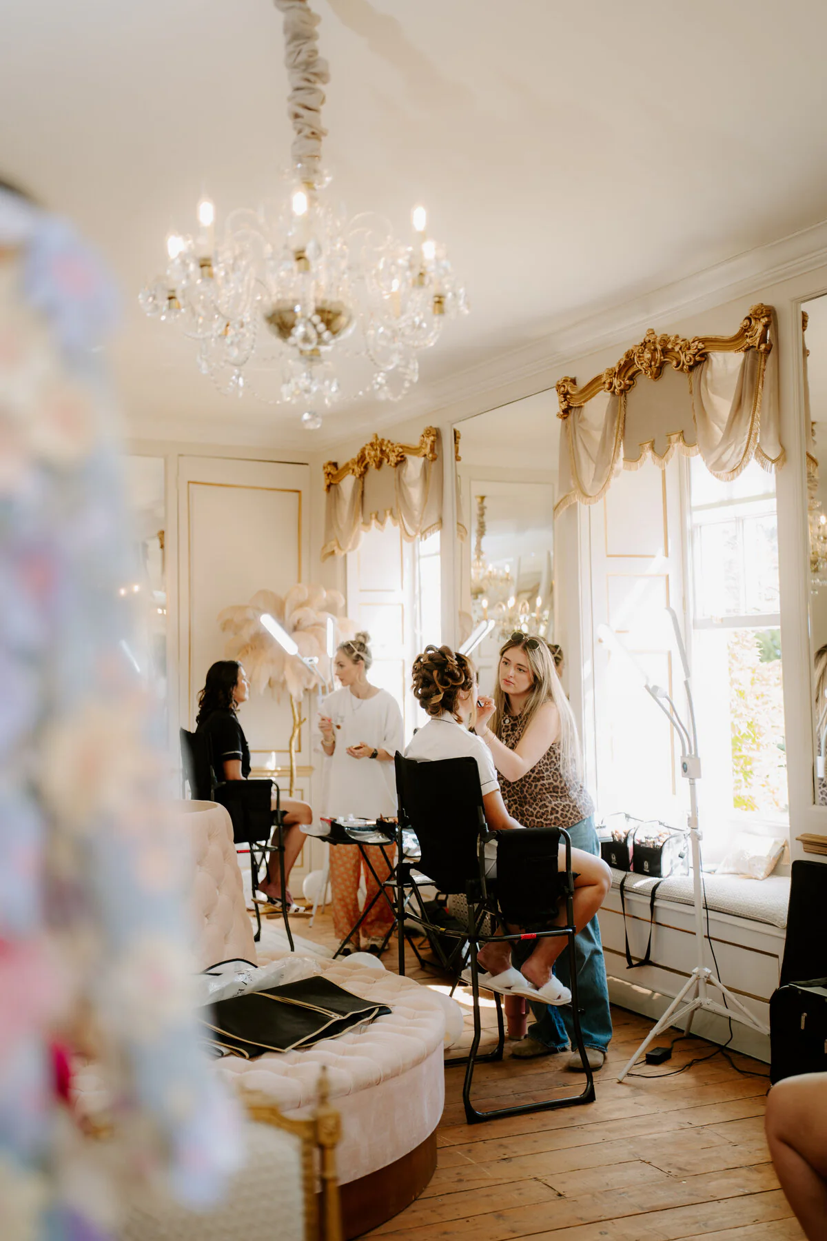 Makeup artist applying bridal makeup in an ornate chandelier-lit manor room.