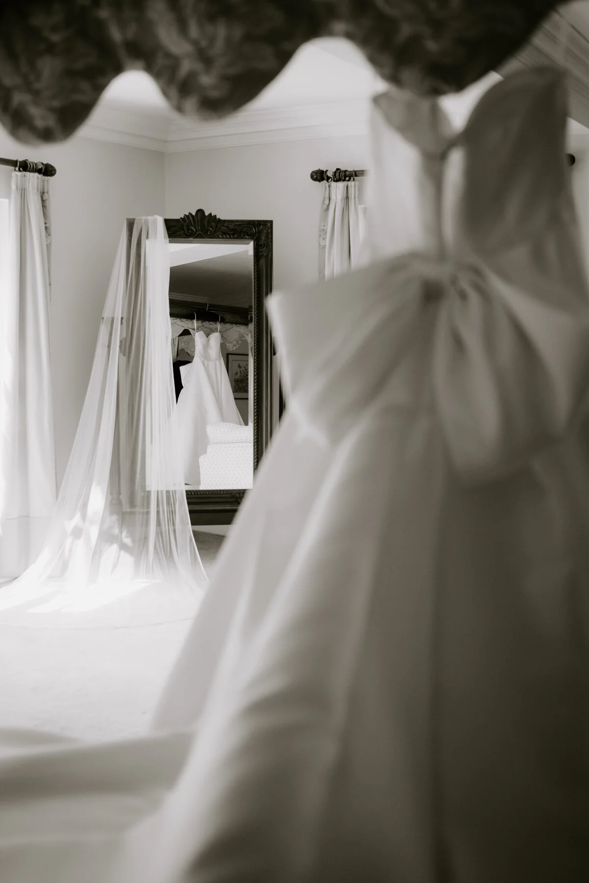 Black and white photograph of a wedding dress and veil reflected in a bedroom mirror.