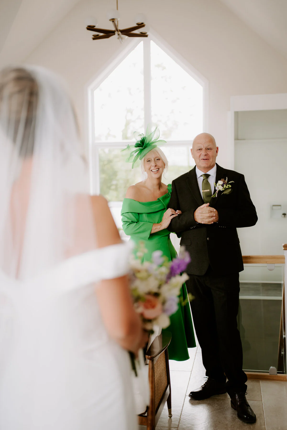 Parents seeing the bride for the first time, her mother in a green dress and fascinator.