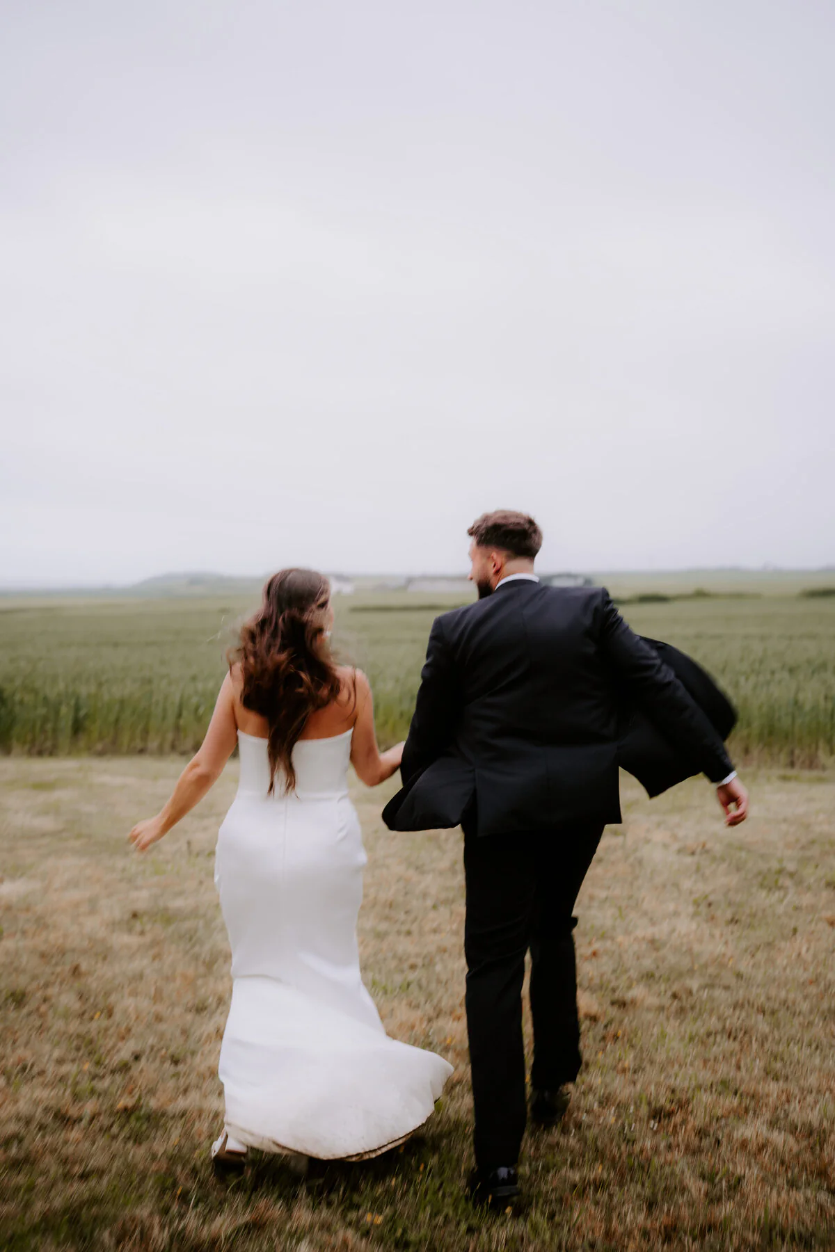 Couple running hand in hand across a rain-soaked field.