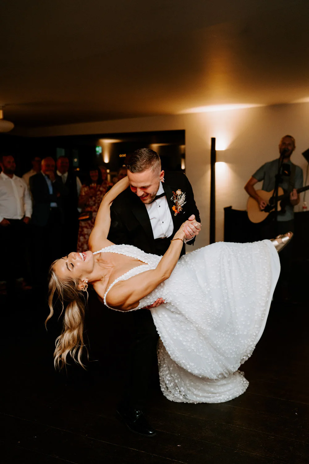 Groom dipping the bride low during their first dance as a musician plays guitar.