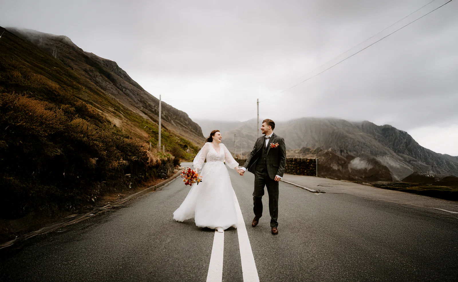 Newlyweds walking hand in hand along a mountain road on their wedding day