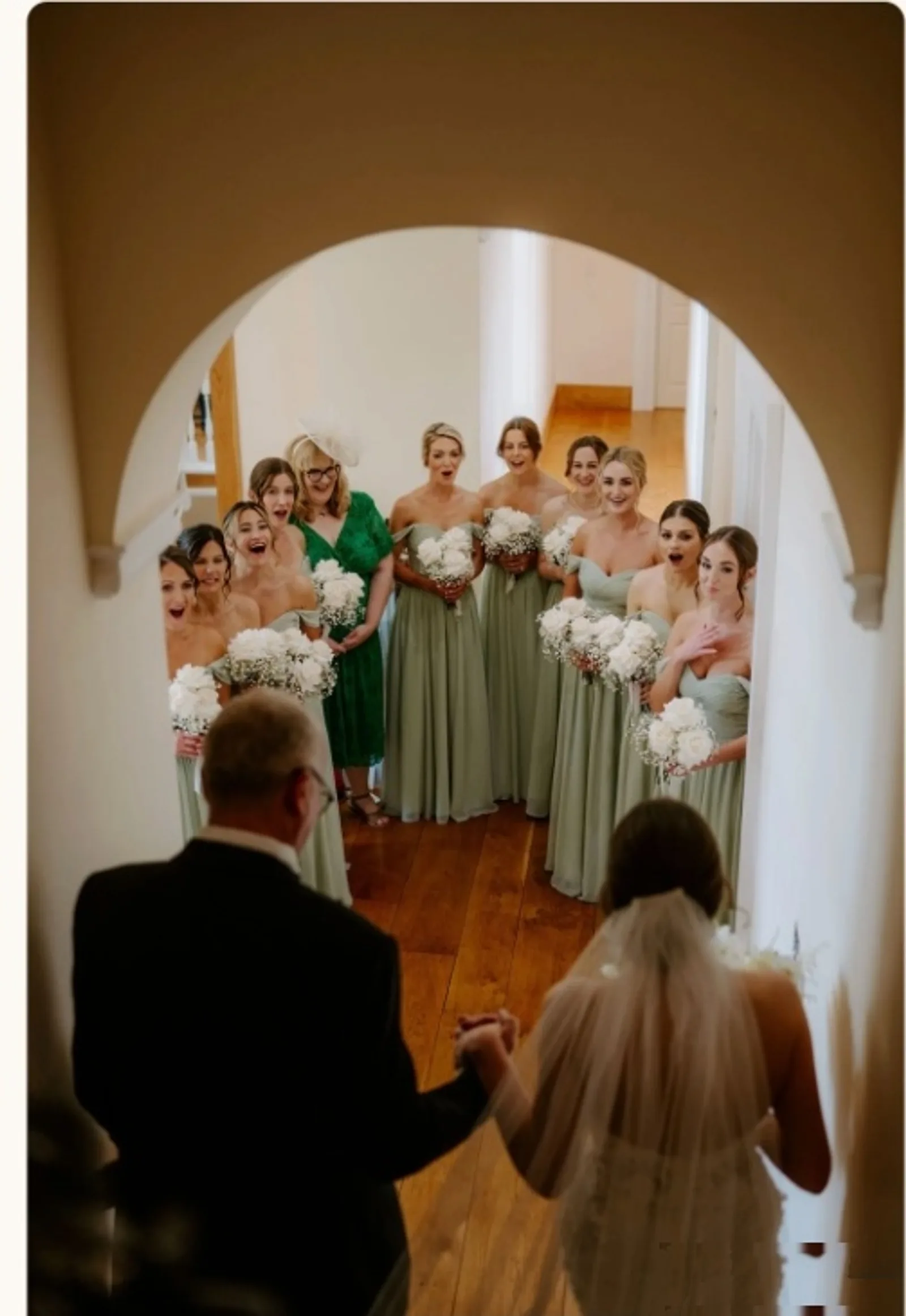 Father of the bride walking with the bride through the stone archway at Notley Abbey as bridesmaids react with joy