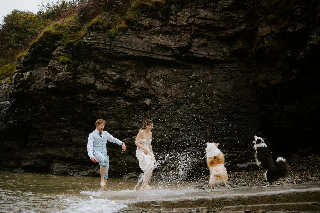 Alicia and Martin playing in the shallow sea with their dogs beneath the coastal rocks